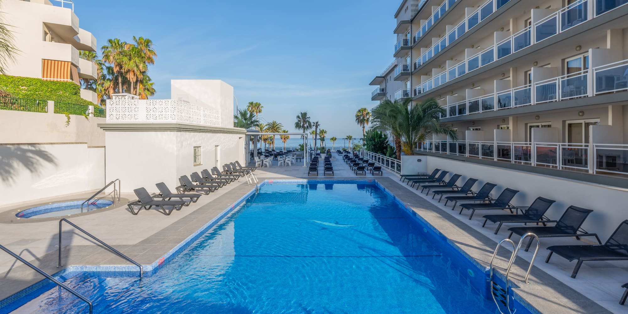 a swimming pool with chairs and a building with palm trees