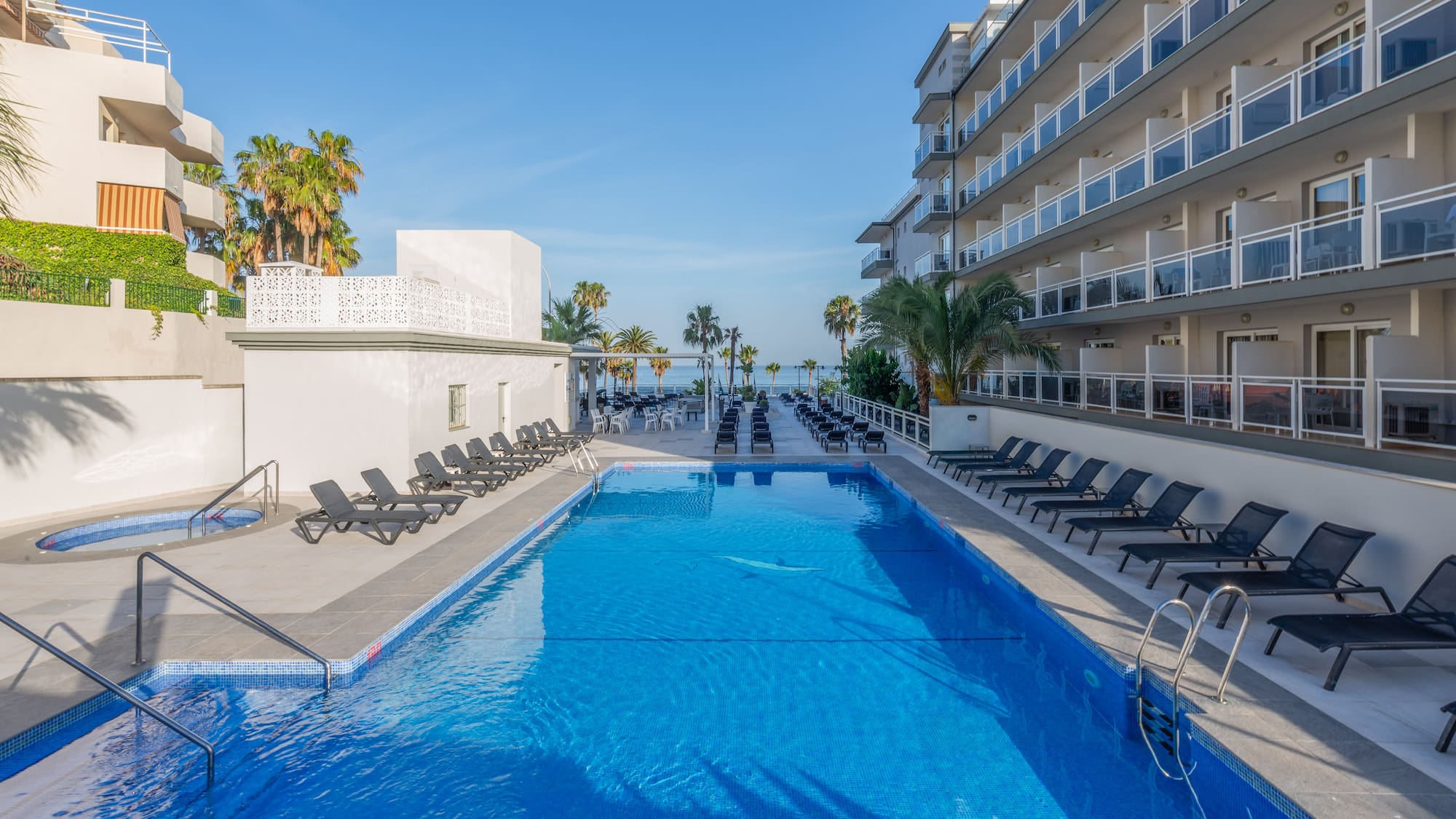 a swimming pool with chairs and a building with palm trees