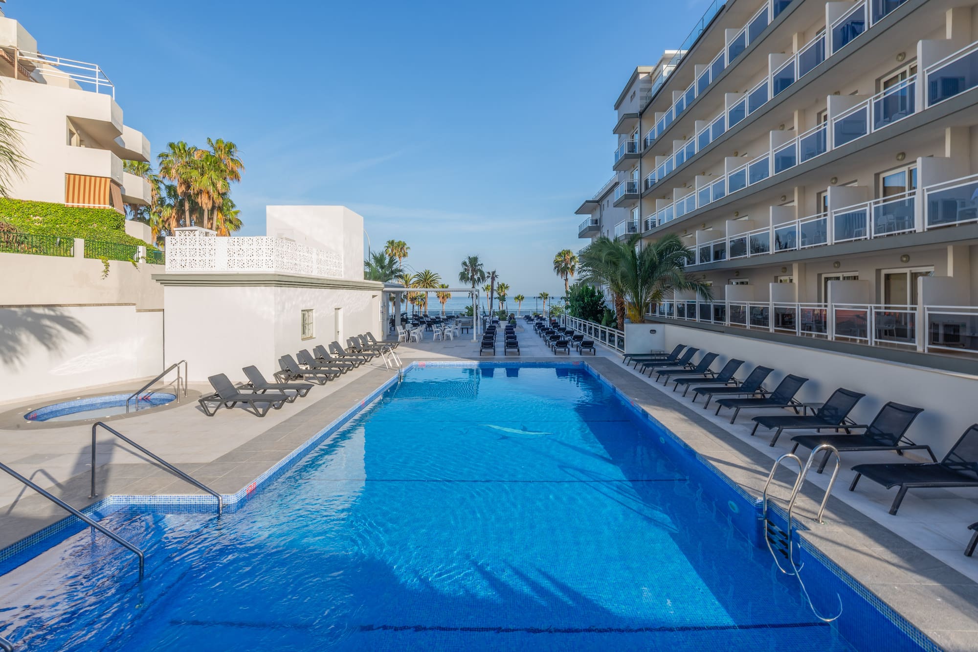 a swimming pool with chairs and a building with palm trees