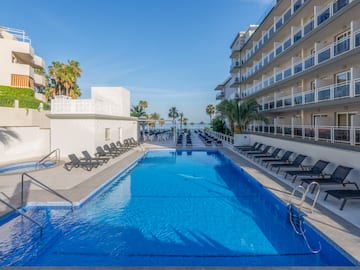 a swimming pool with chairs and a building with palm trees