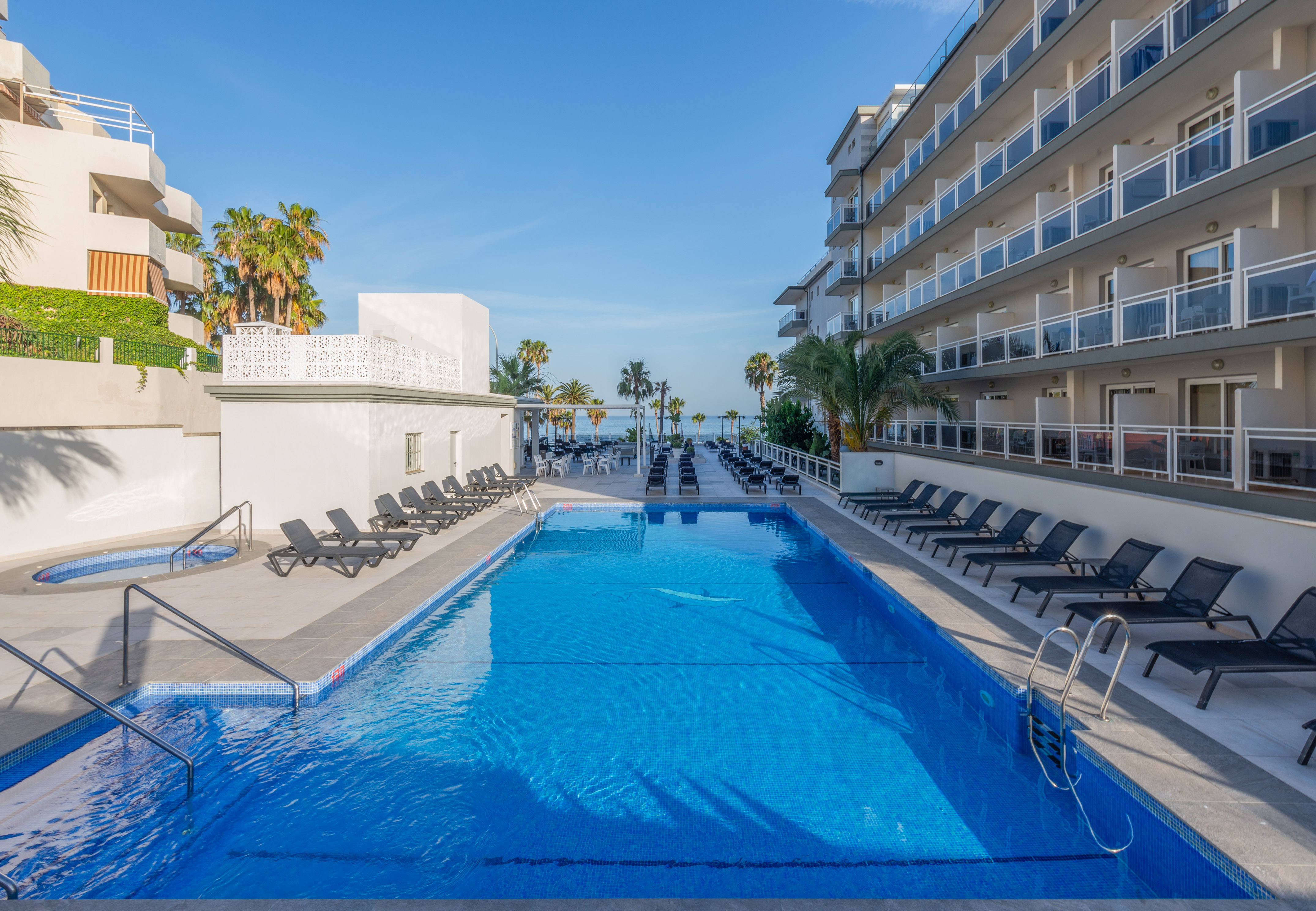 a swimming pool with chairs and a building with palm trees