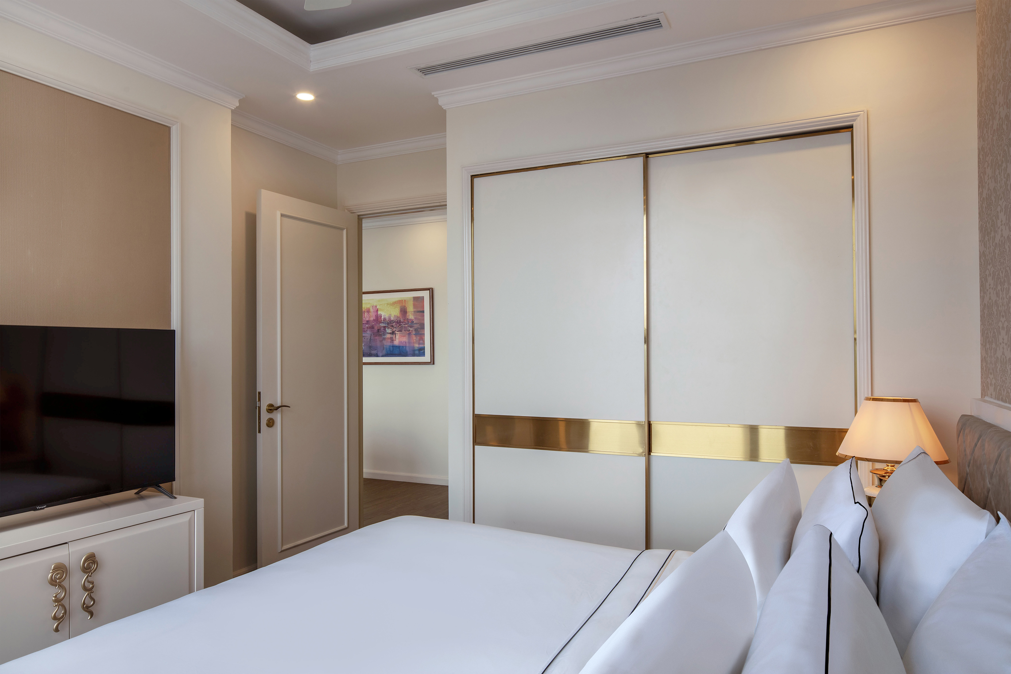 Luxury bedroom with white bed, gold sliding closet, and TV.
