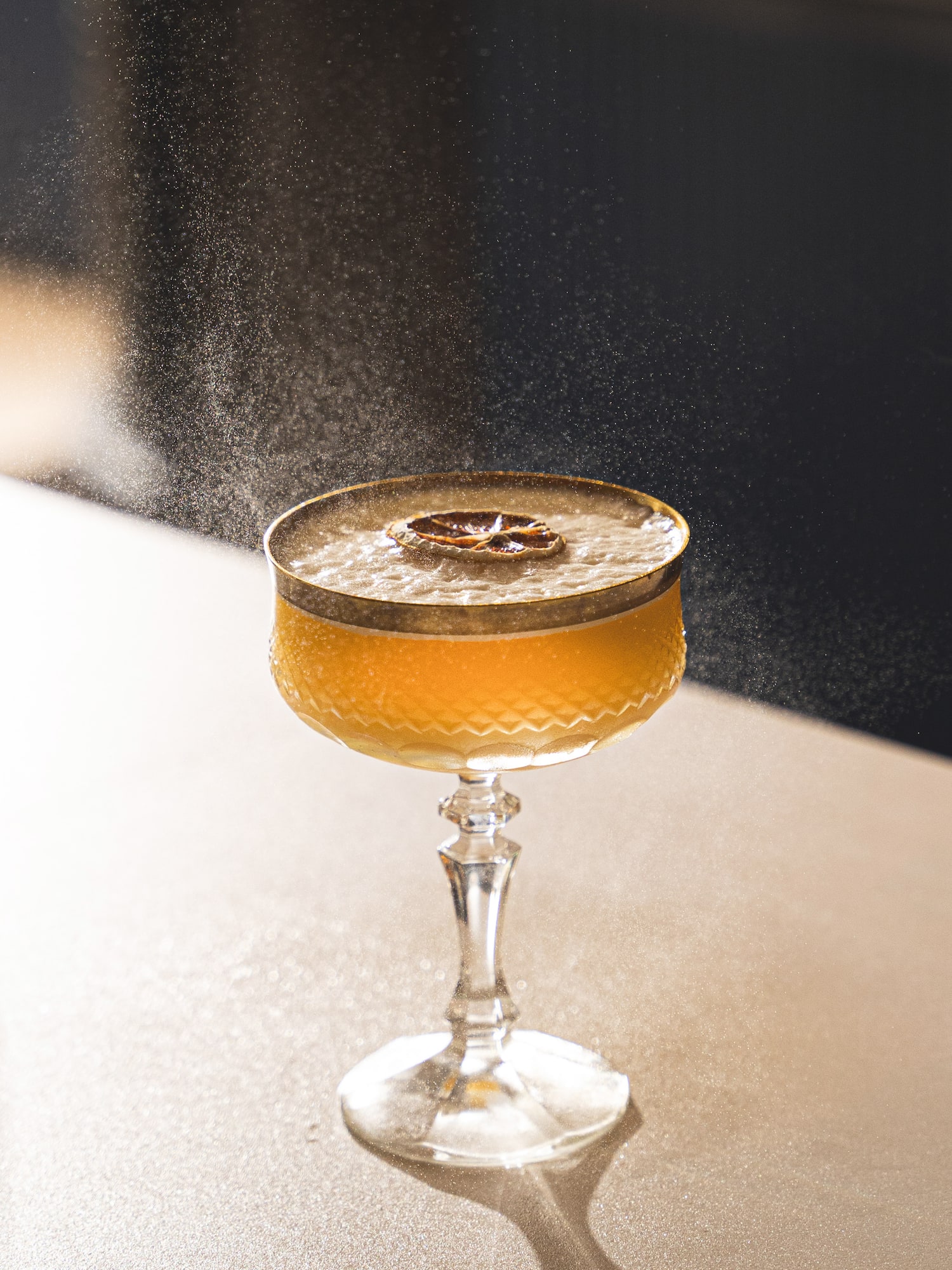Orange cocktail in coupe glass with dried citrus garnish and fine spray.