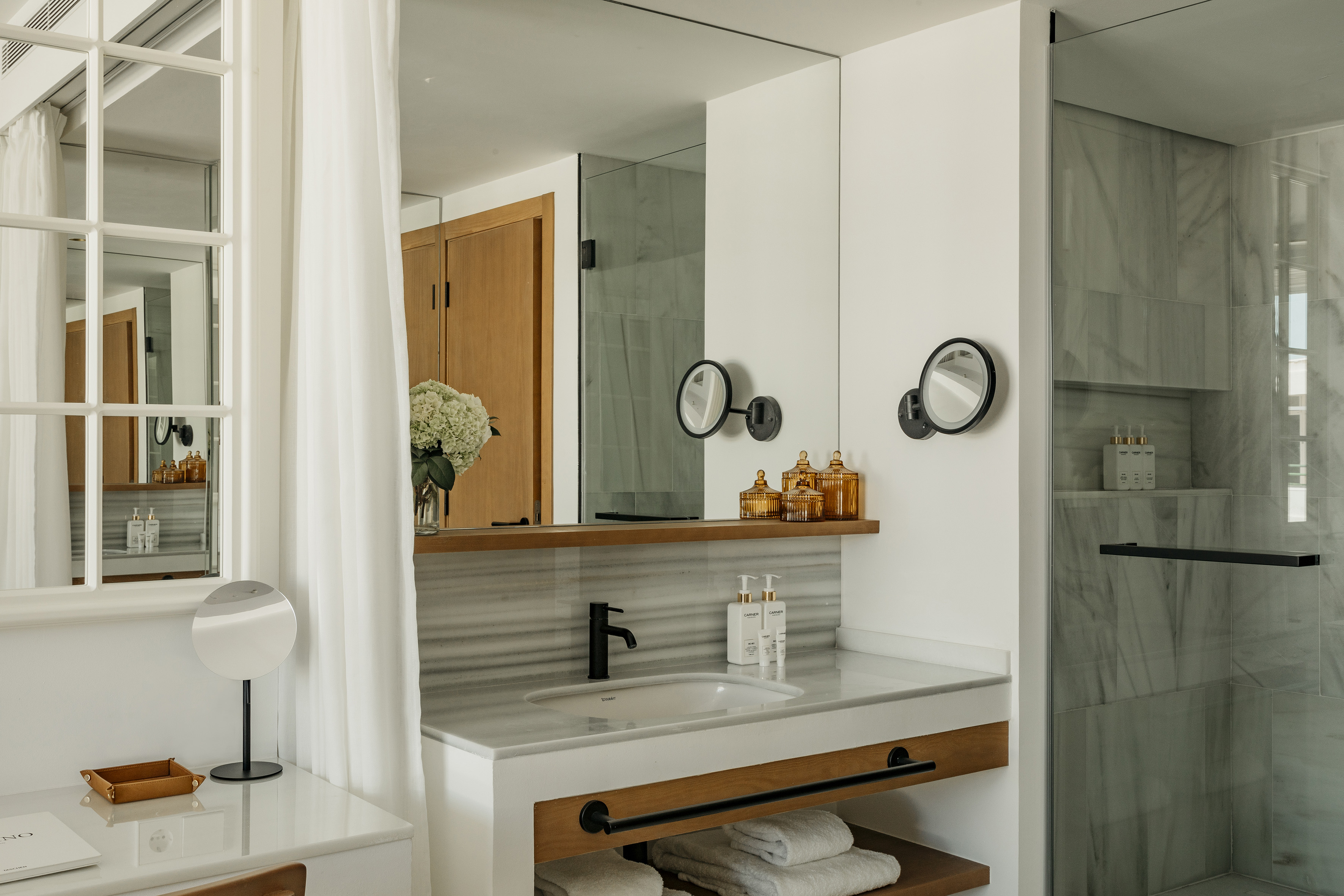 Modern hotel bathroom with marble vanity, black faucet, and glass shower.