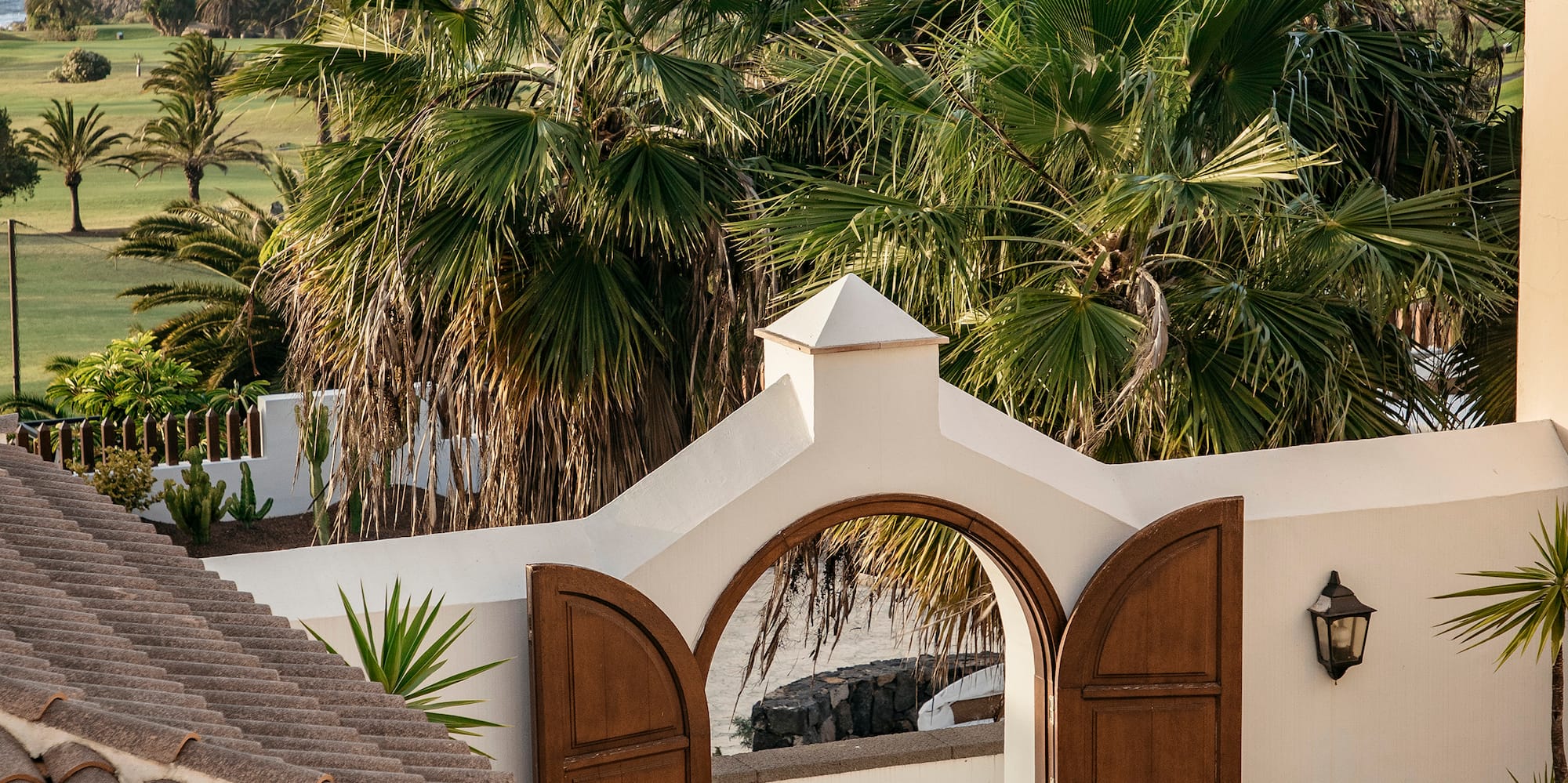 White villa archway overlooking tropical ocean, palm trees, and coastal golf course.
