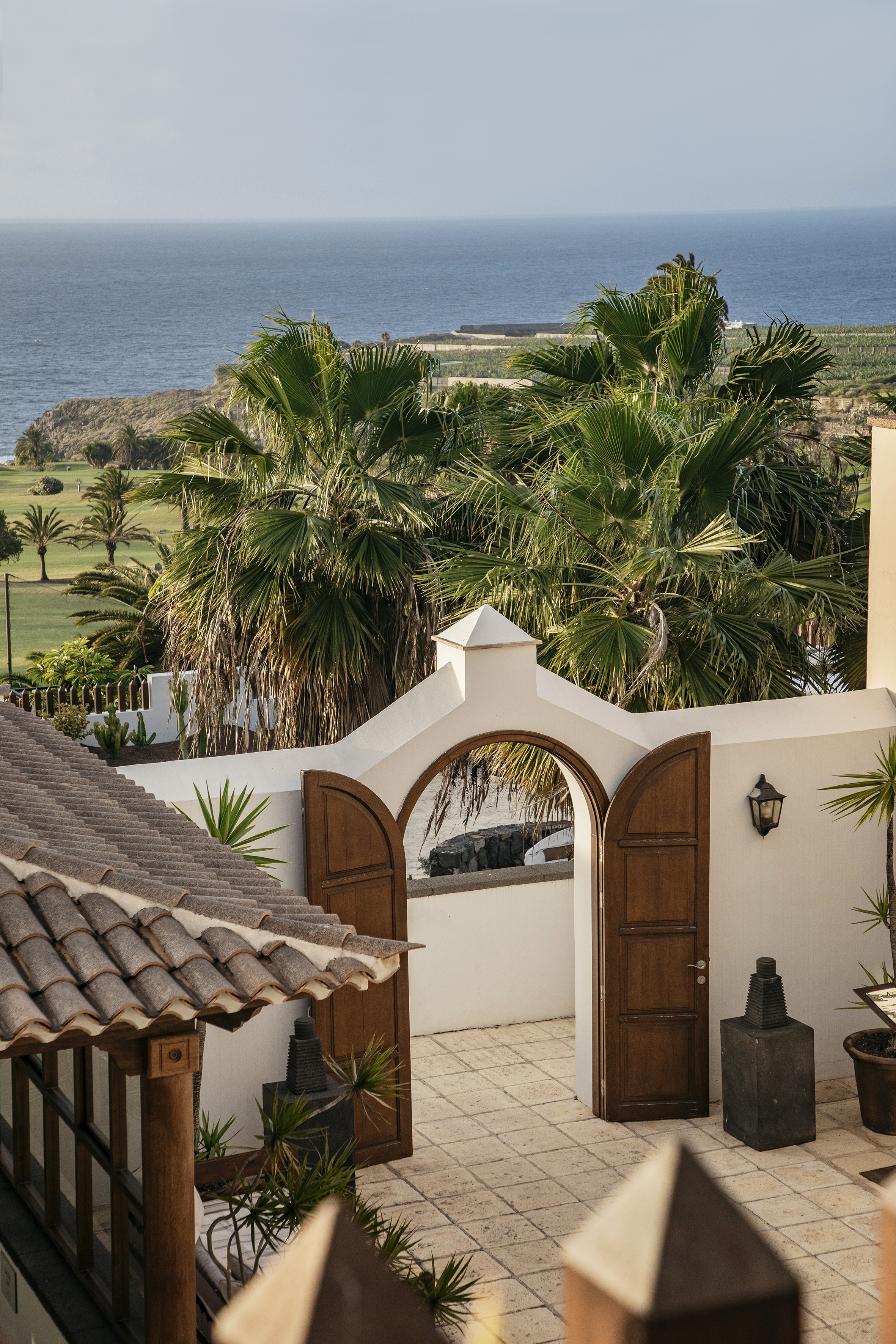 White villa archway overlooking tropical ocean, palm trees, and coastal golf course.