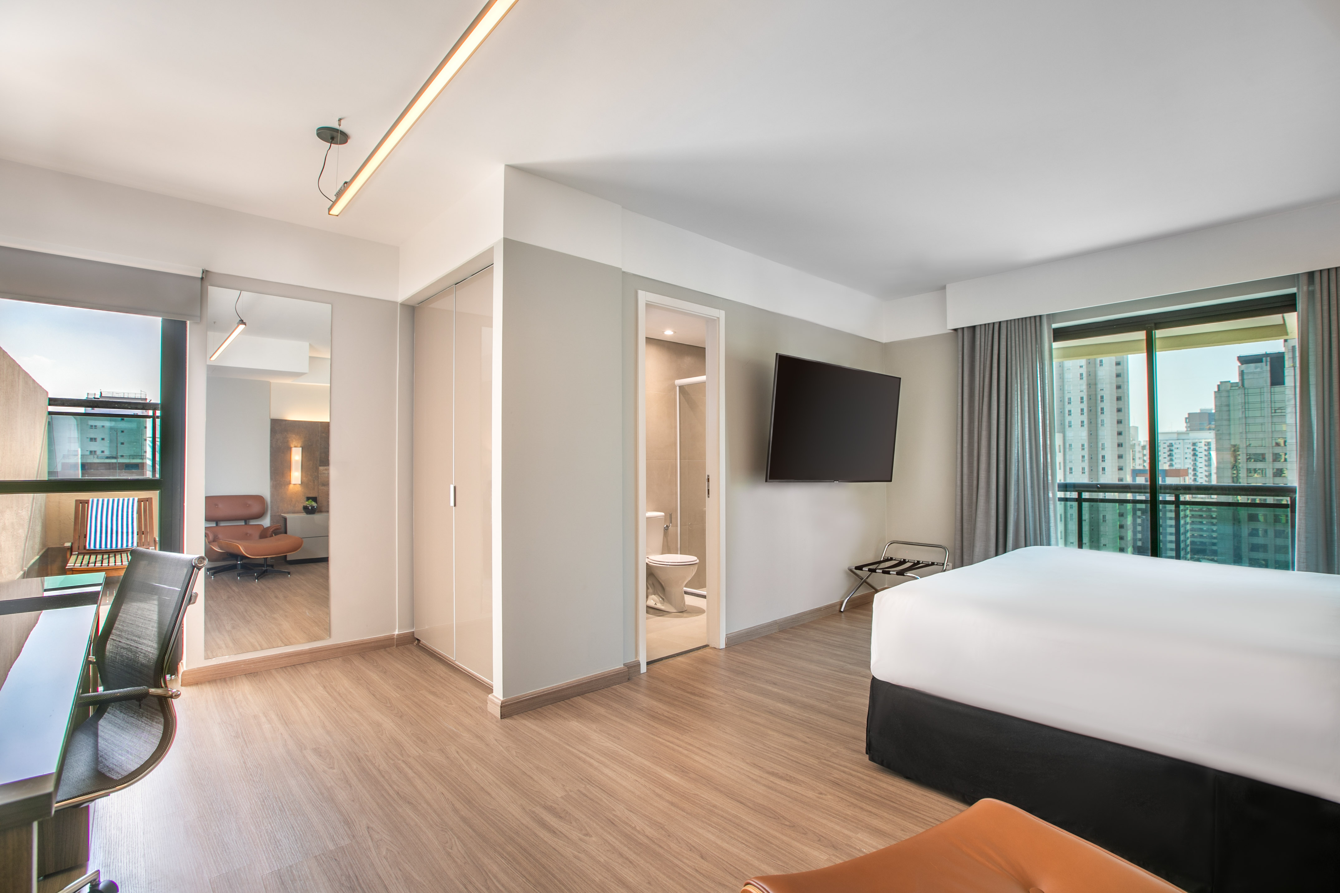 Modern hotel room with bed, wall TV, desk, bathroom, and city view.