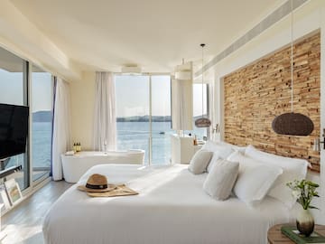 a bedroom with a bathtub and a large window overlooking the water