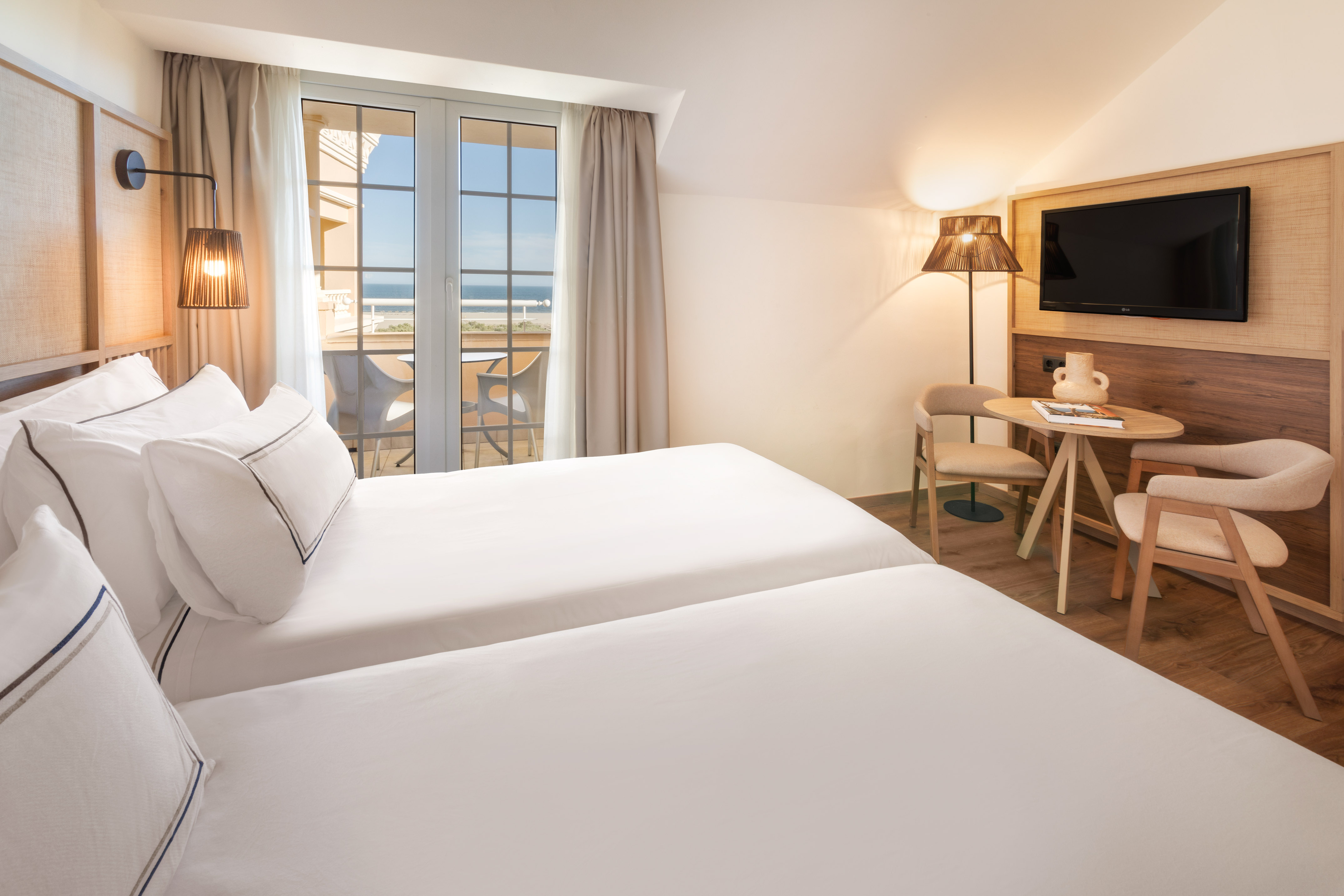Modern hotel room with twin beds, ocean view balcony, and a cozy sitting area.