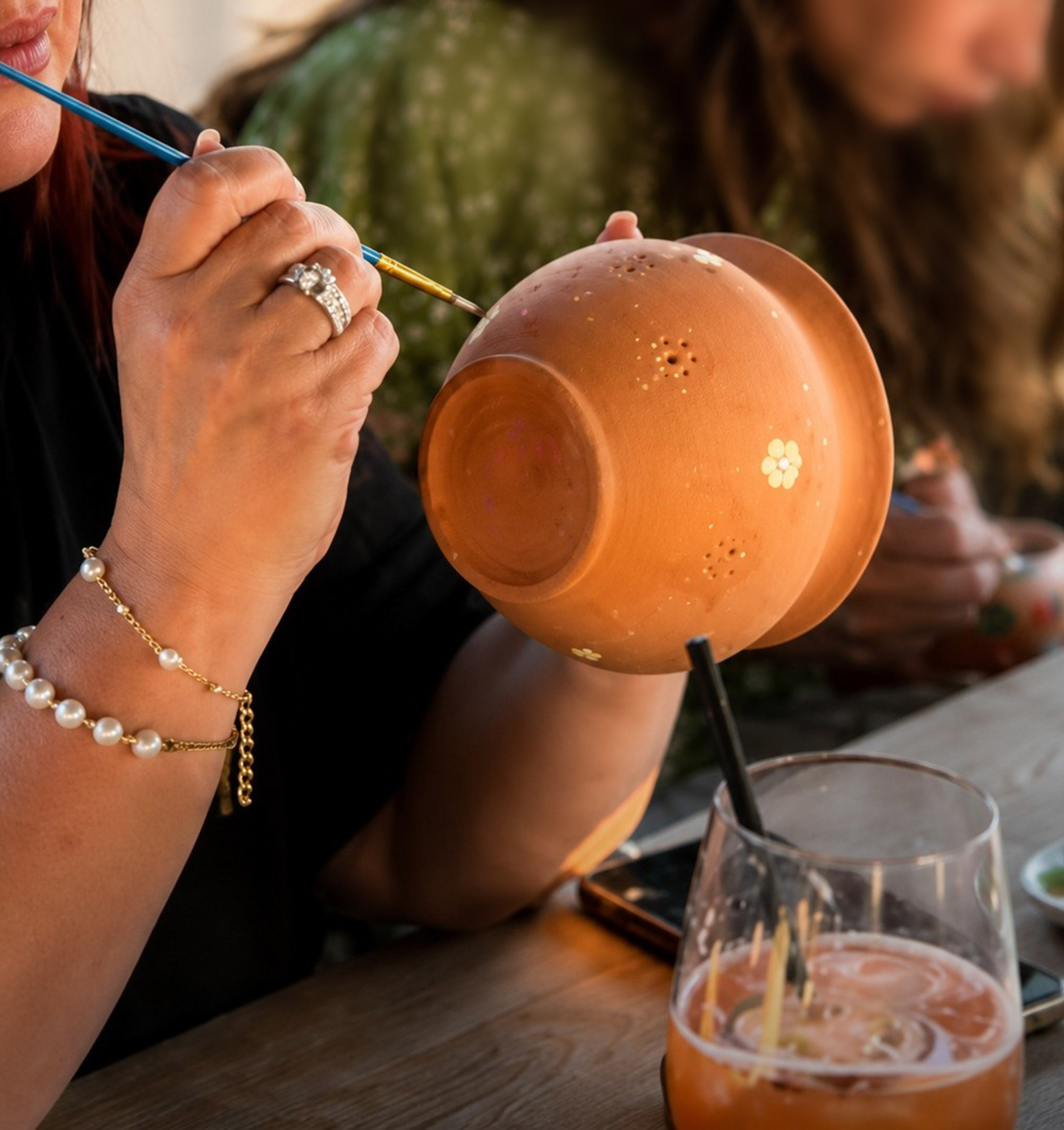 Hand painting white floral designs on a terracotta pot at a craft event.