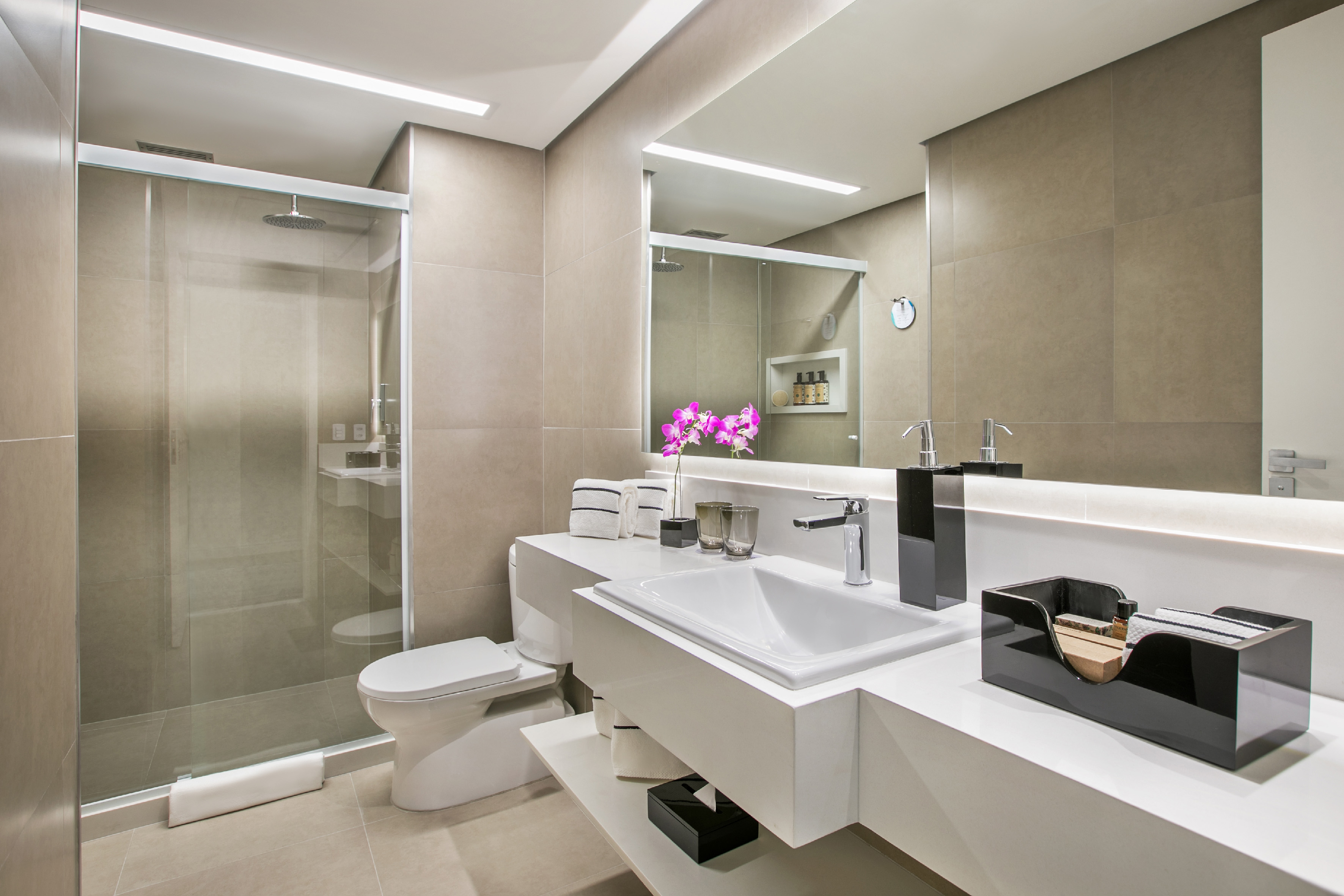 Modern hotel bathroom with glass shower, toilet, and lit vanity mirror.