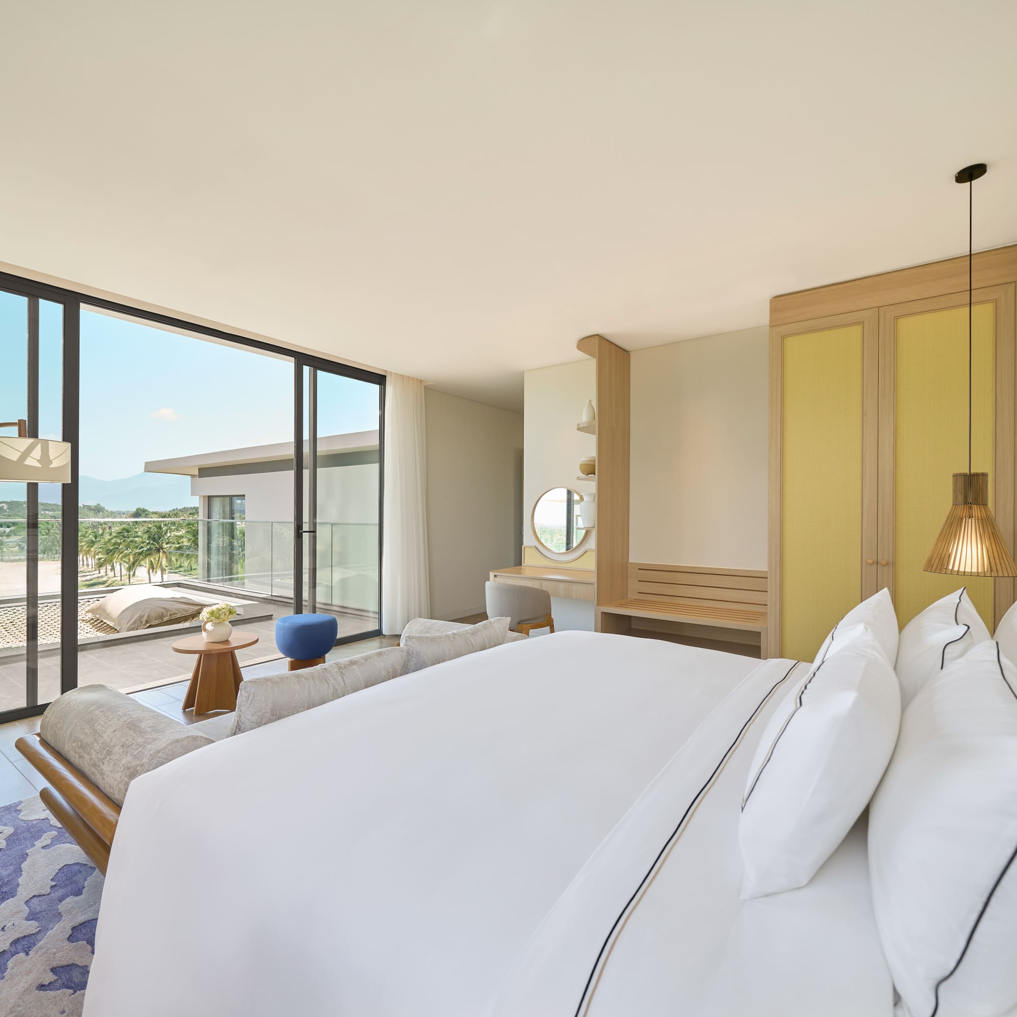 Luxury resort bedroom with balcony, large bed, and tropical landscape view.