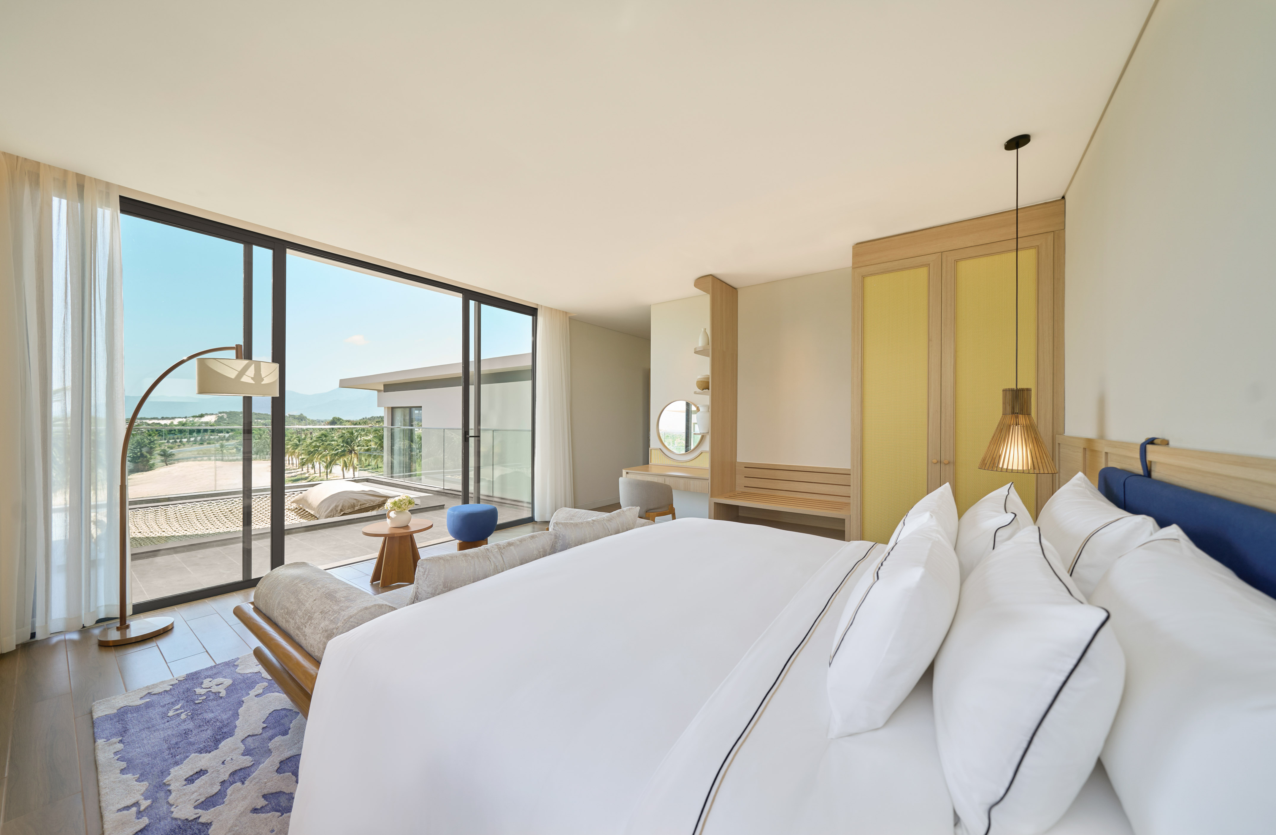 Luxury resort bedroom with balcony, large bed, and tropical landscape view.