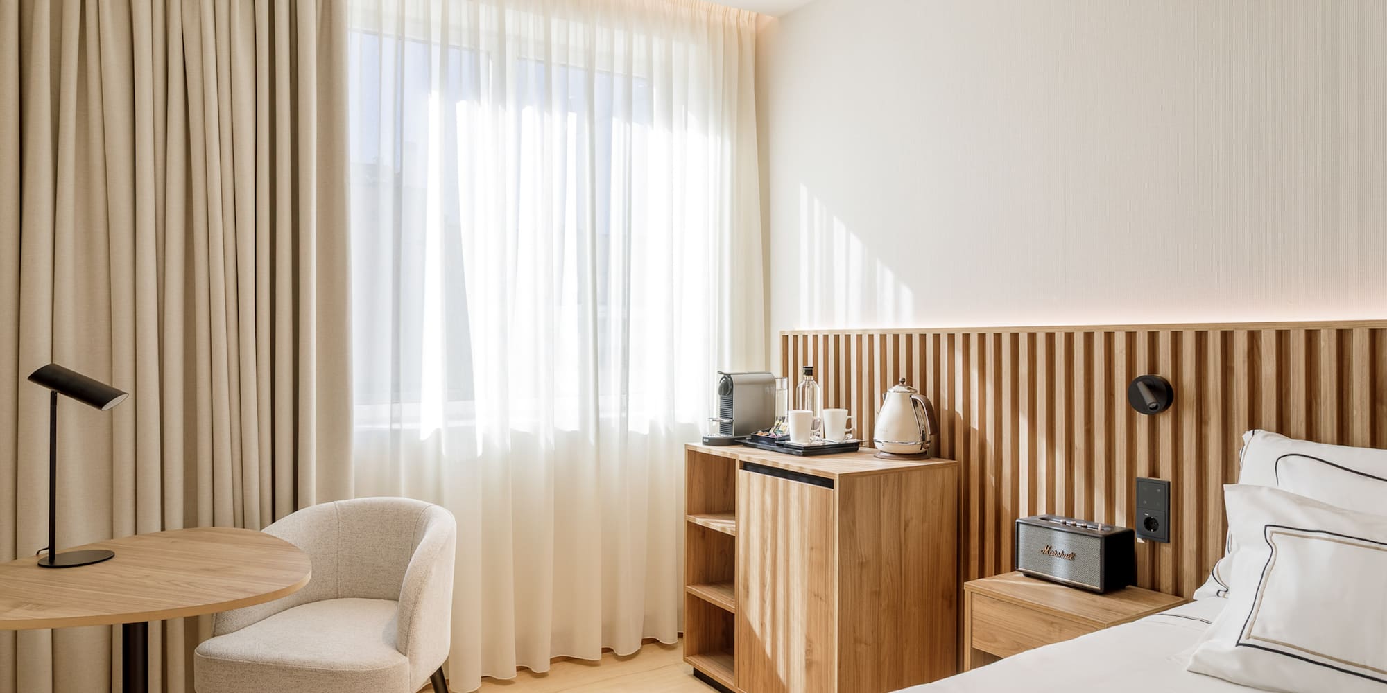 Modern hotel bedroom with light wood, neutral decor, and coffee amenities.