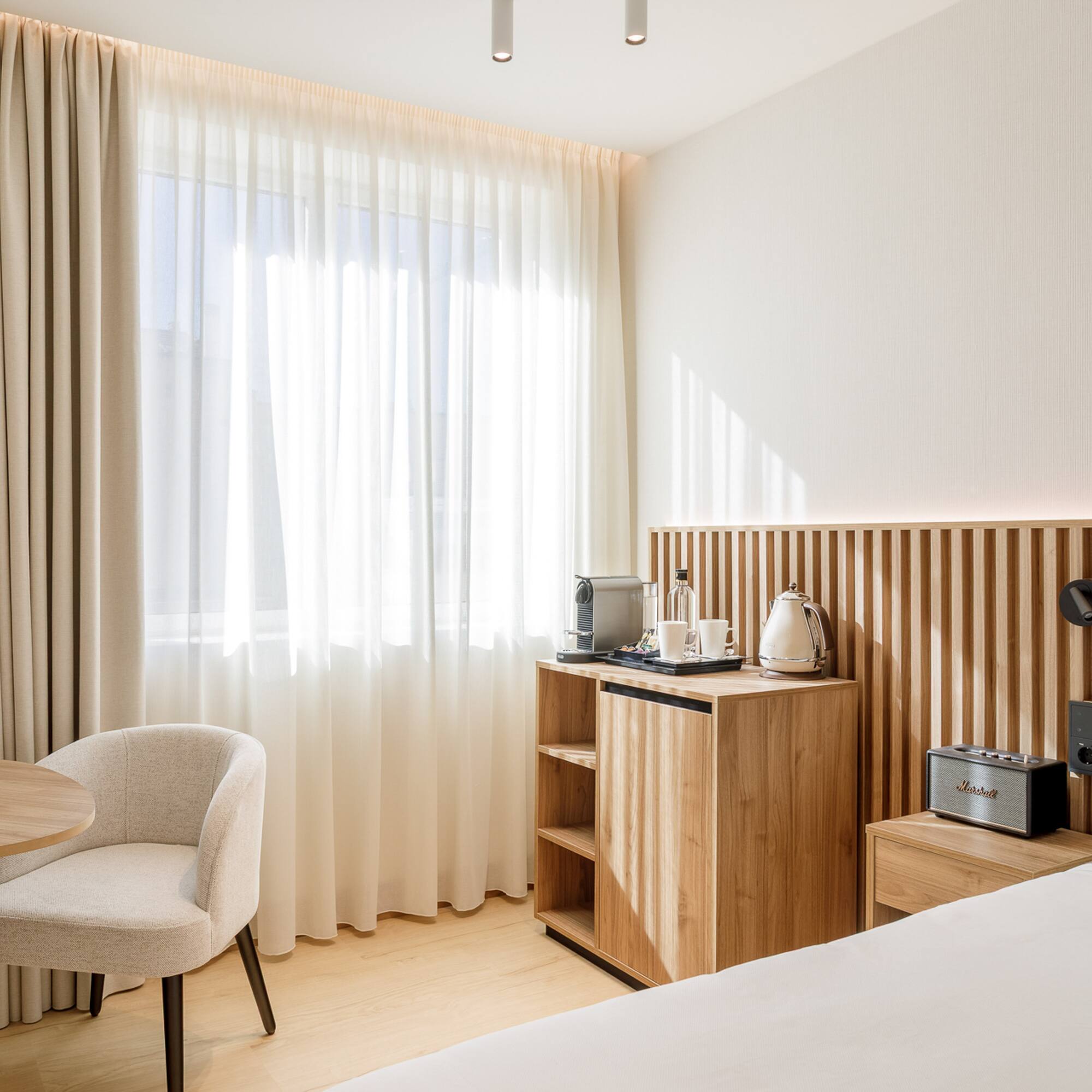 Modern hotel bedroom with light wood, neutral decor, and coffee amenities.