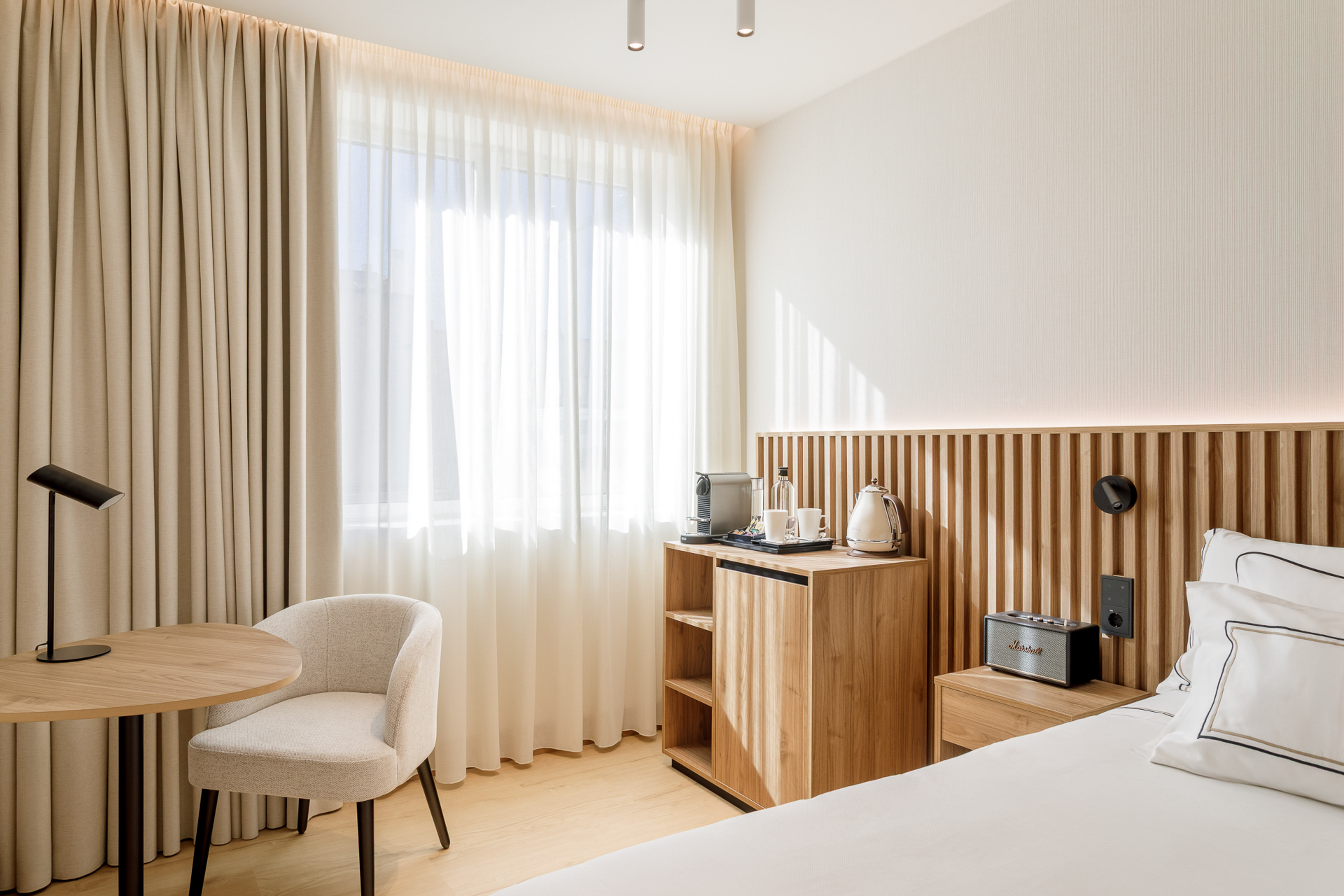 Modern hotel room with wooden headboard, minibar, coffee machine, and table.