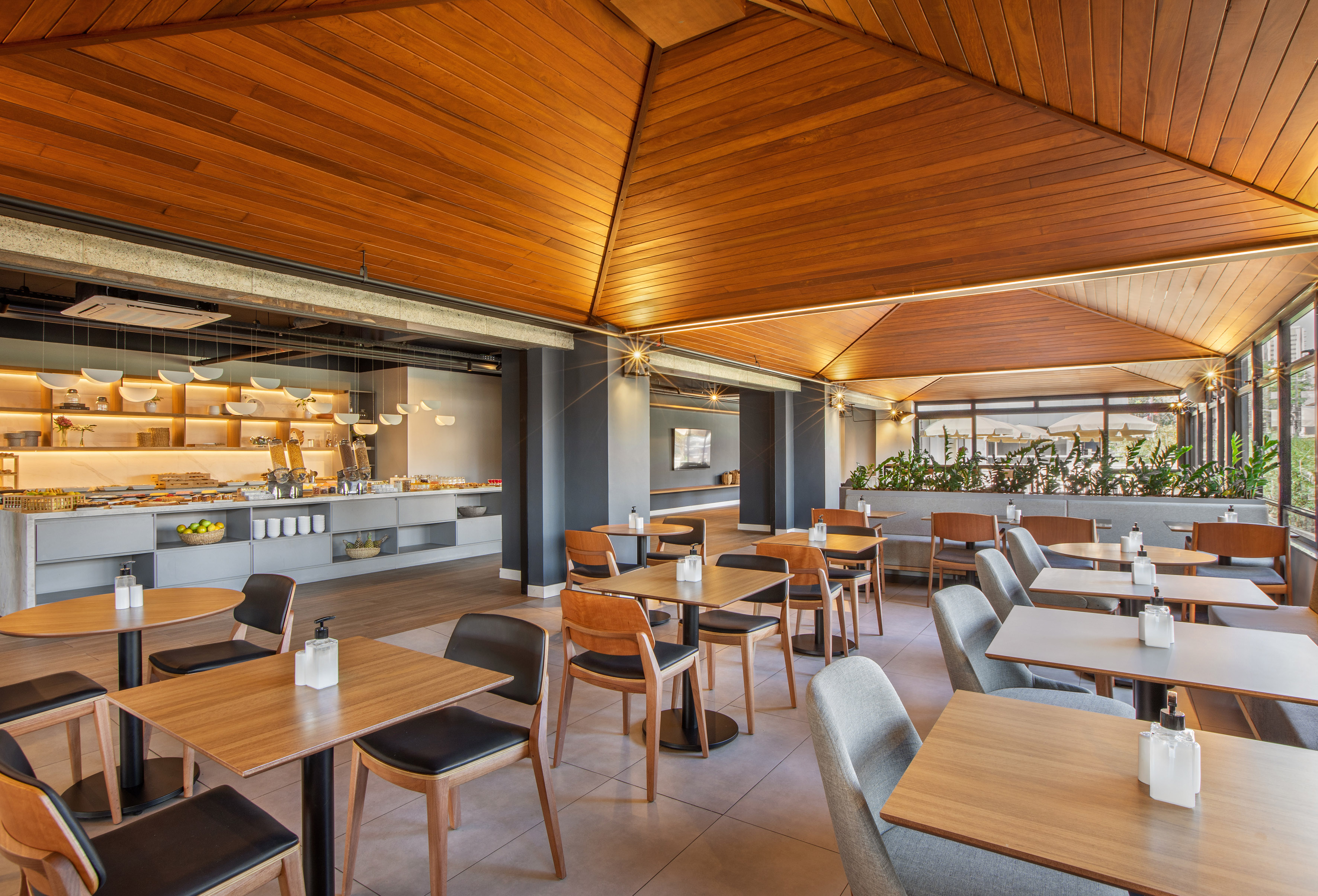 Hotel breakfast area with a buffet, dining tables, and warm wooden ceiling.