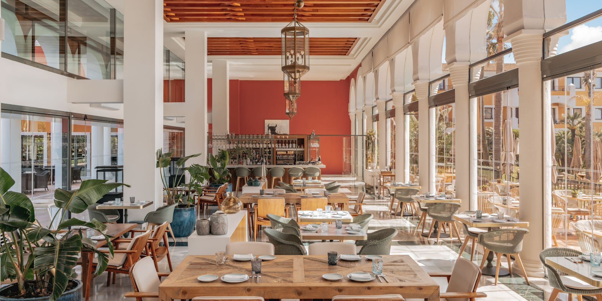 Spacious Mediterranean restaurant with wooden tables, bar, and arch windows.