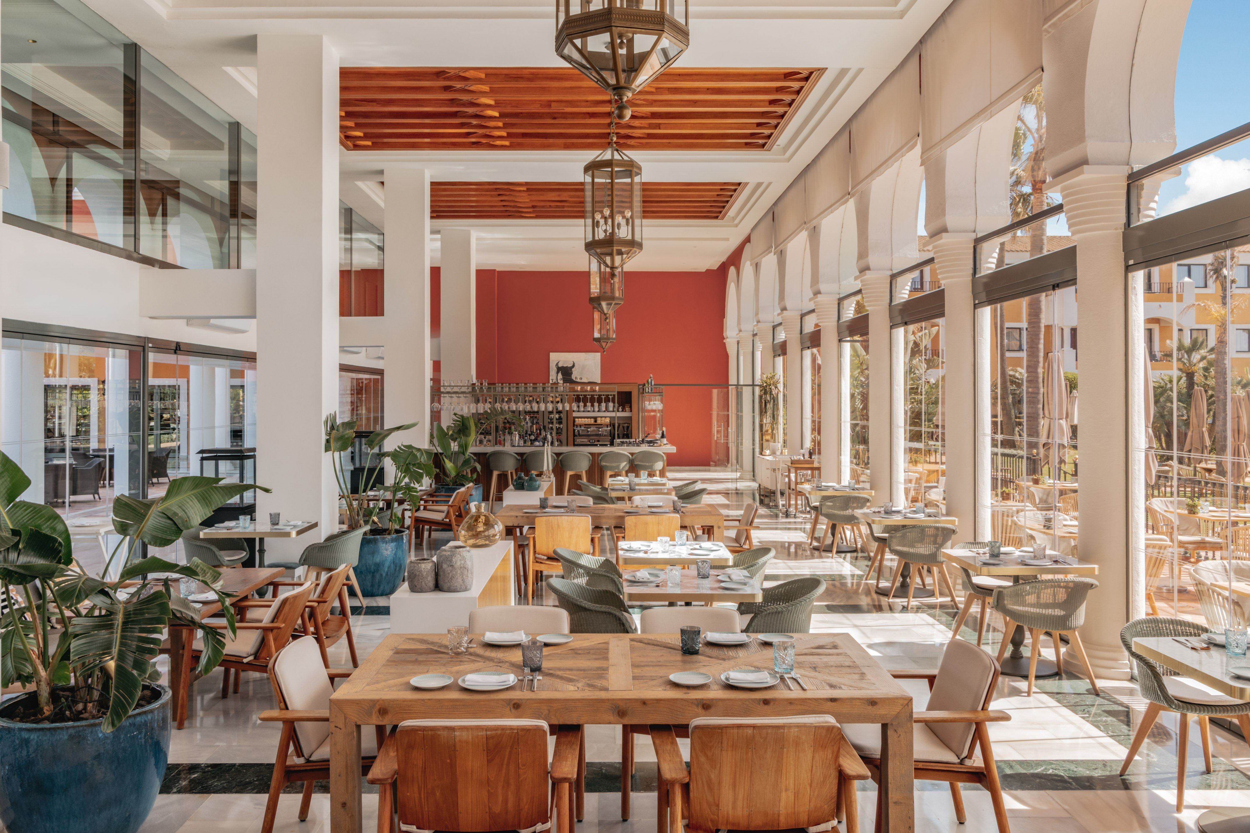 Spacious Mediterranean restaurant with wooden tables, bar, and arch windows.