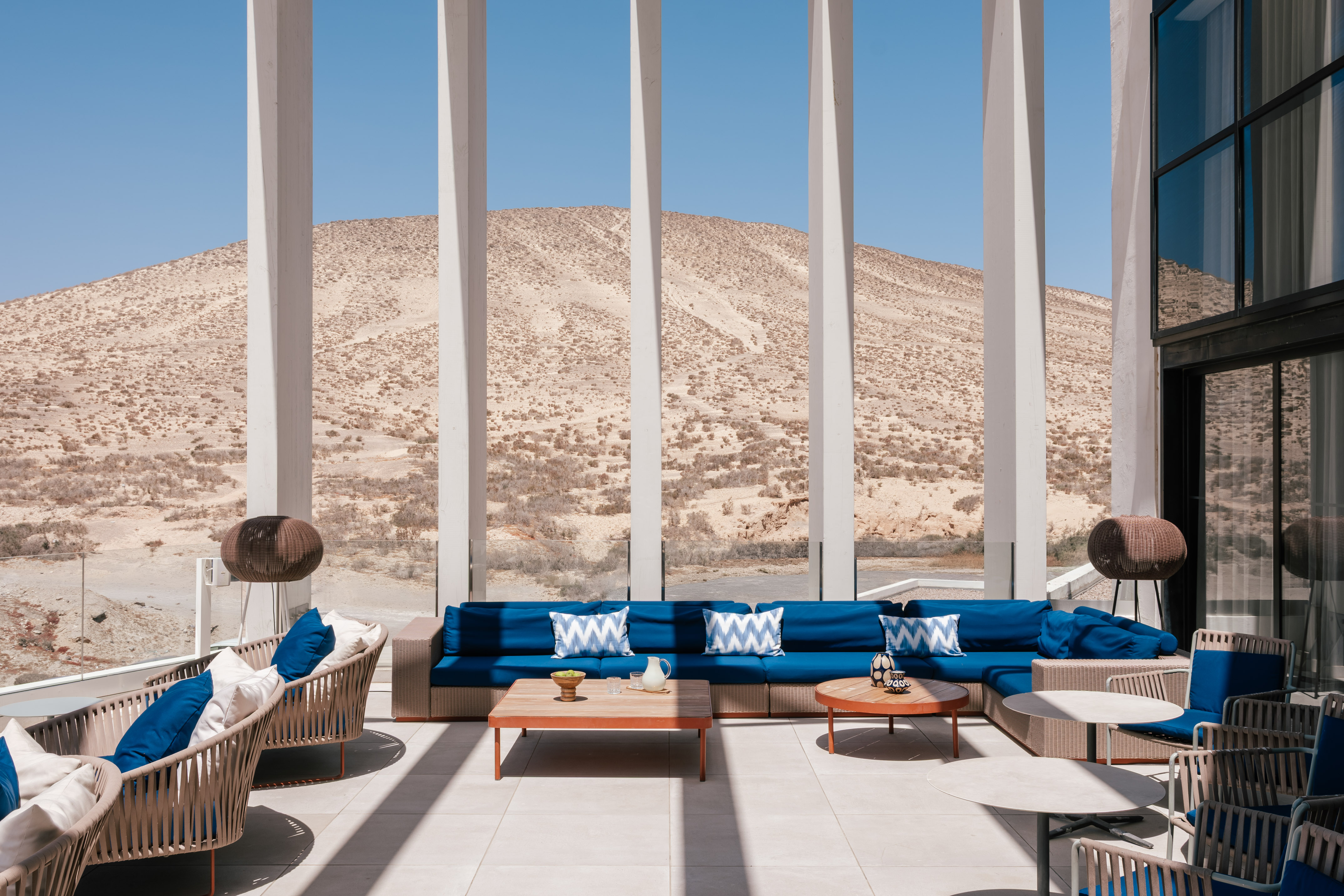 Modern outdoor lounge with blue sofas, coffee tables, and desert mountain view.