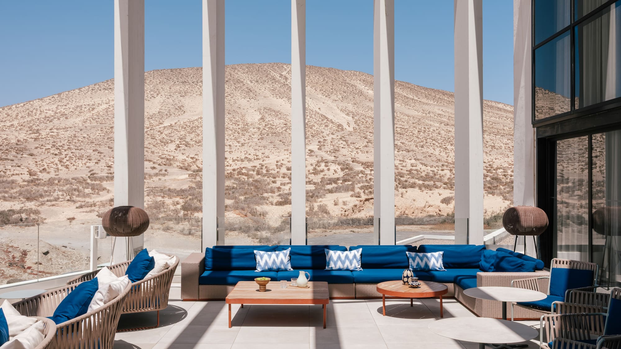 Modern outdoor lounge with blue sofas, coffee tables, and desert mountain view.