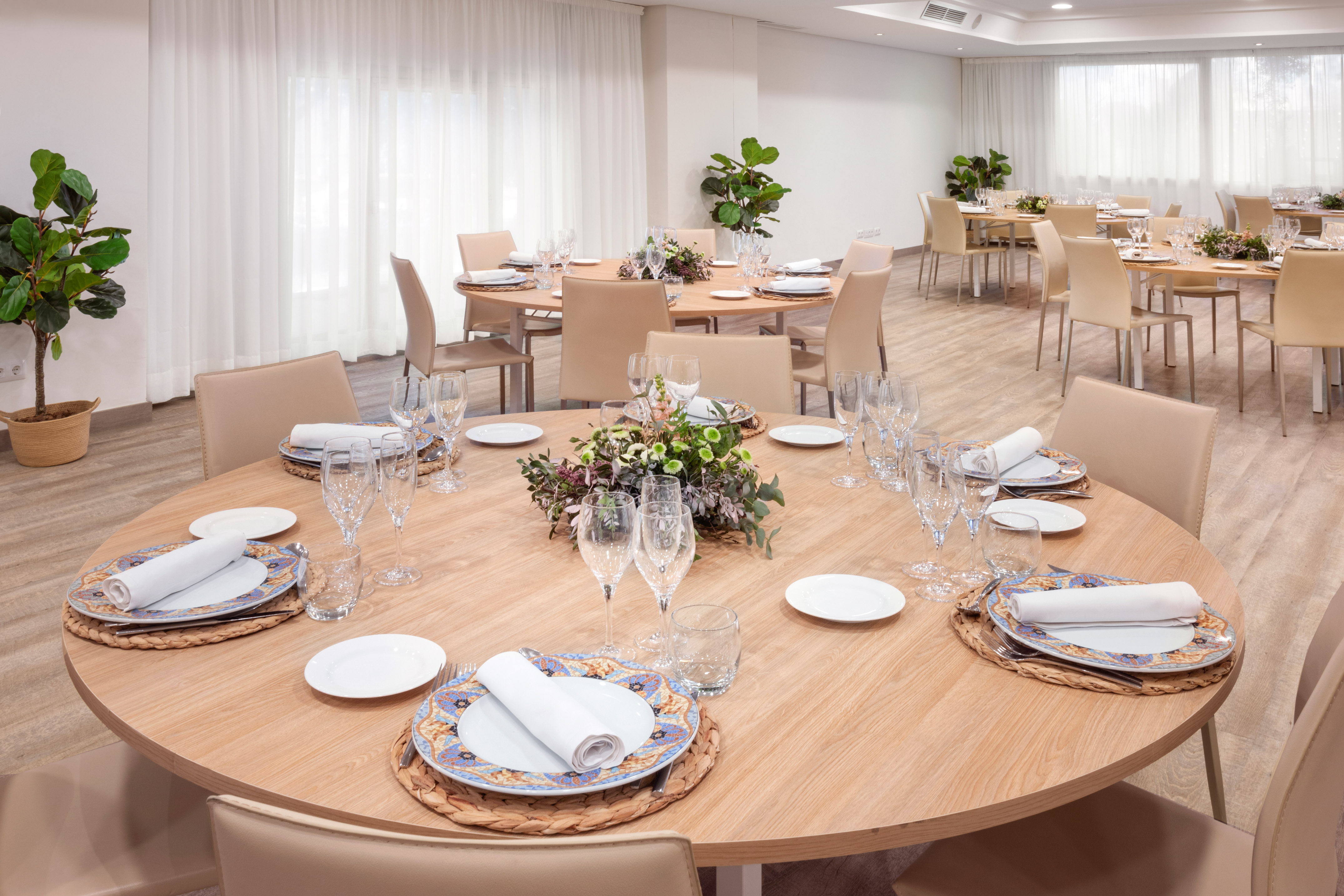 Modern banquet hall with set round dining tables and elegant floral centerpieces.