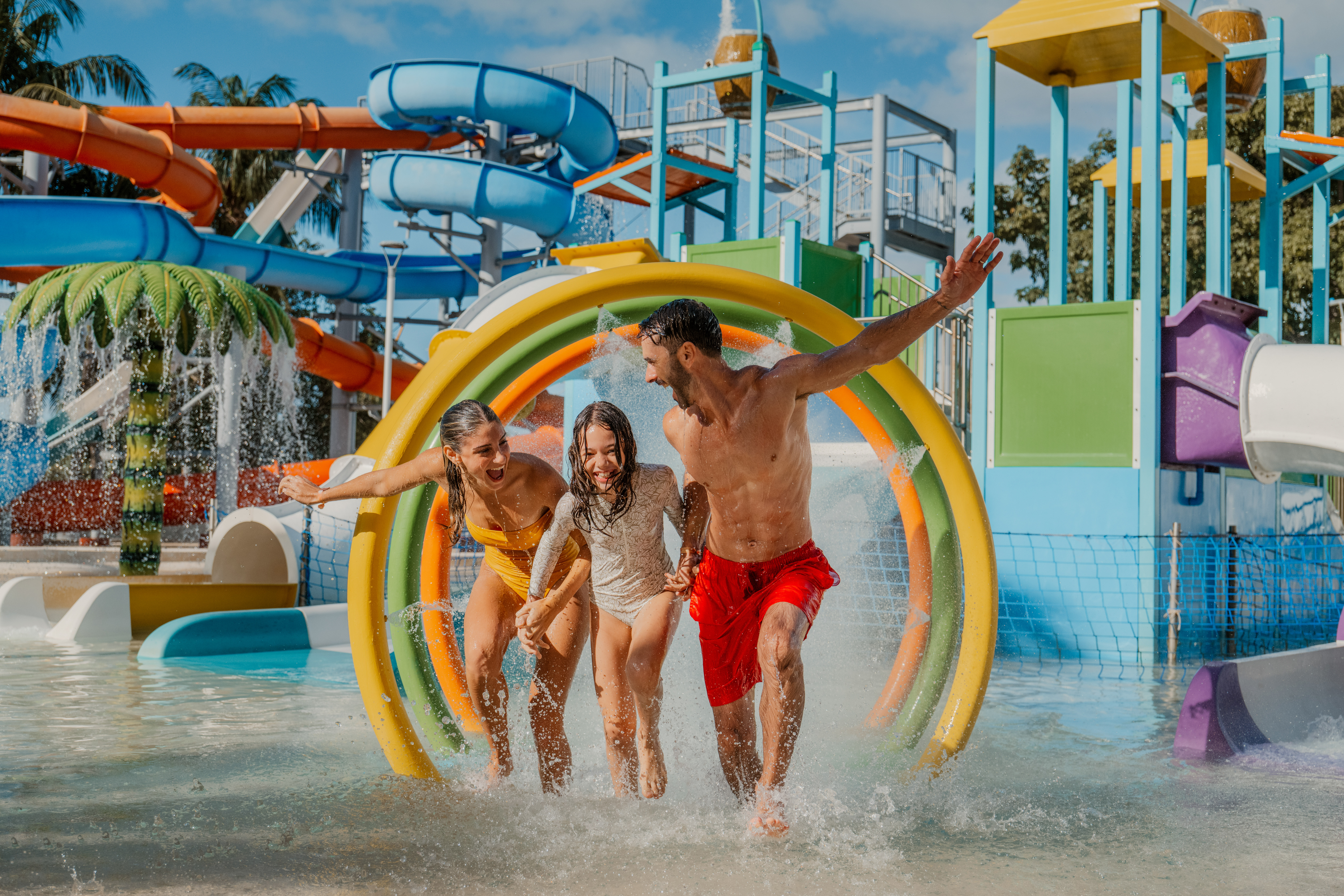 Happy family splashing through a rainbow water feature at a colorful water park.