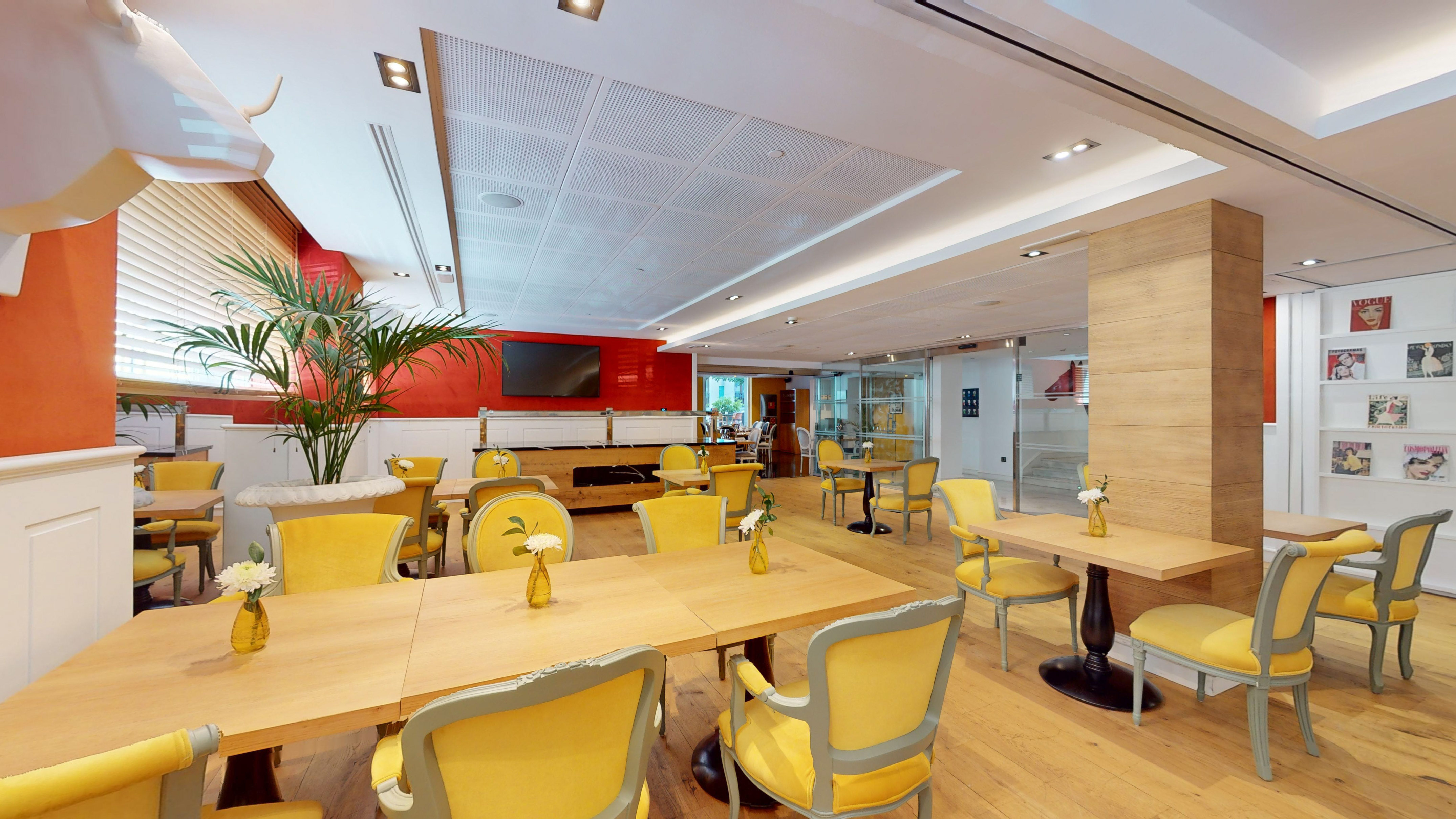 Modern cafe interior with yellow chairs, wood tables, red walls, and plant decor.