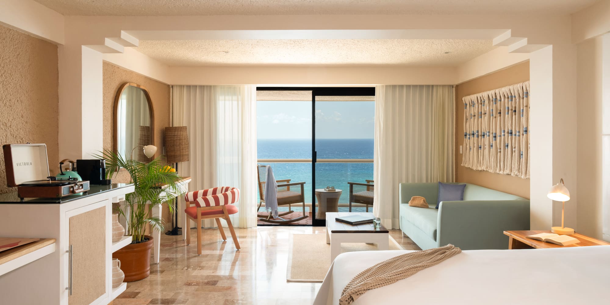 Bright hotel room with ocean view balcony, daybed, and Victrola record player.
