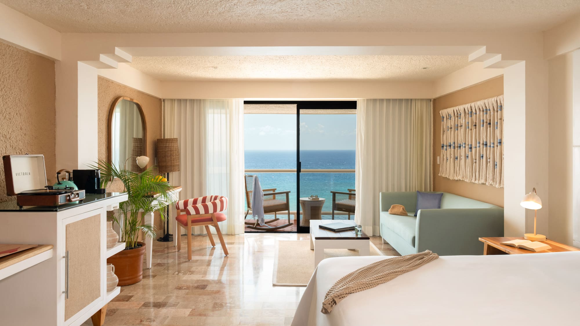 Bright hotel room with ocean view balcony, daybed, and Victrola record player.