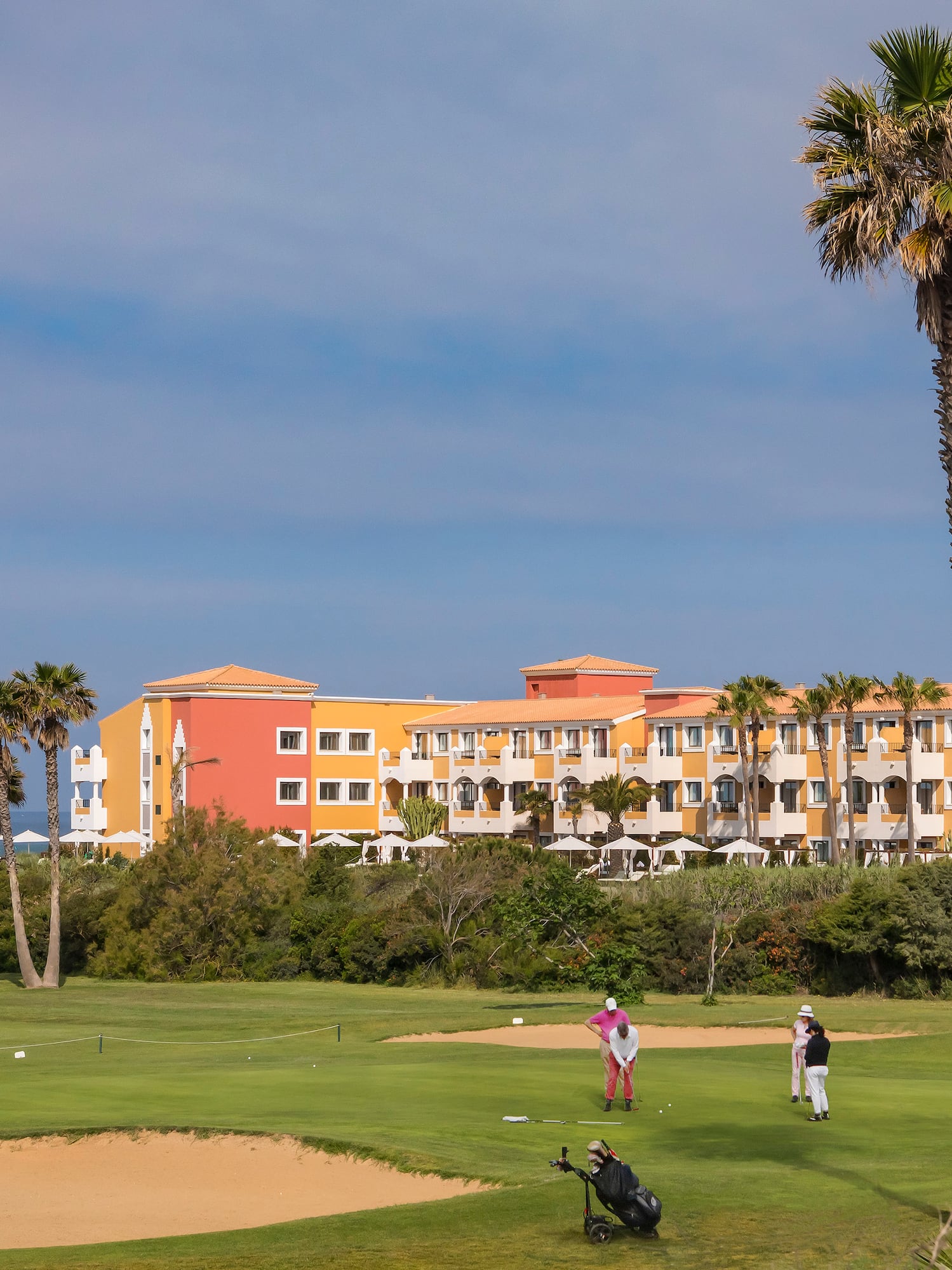 Golfers on tropical golf course with colorful resort hotel and palm trees.