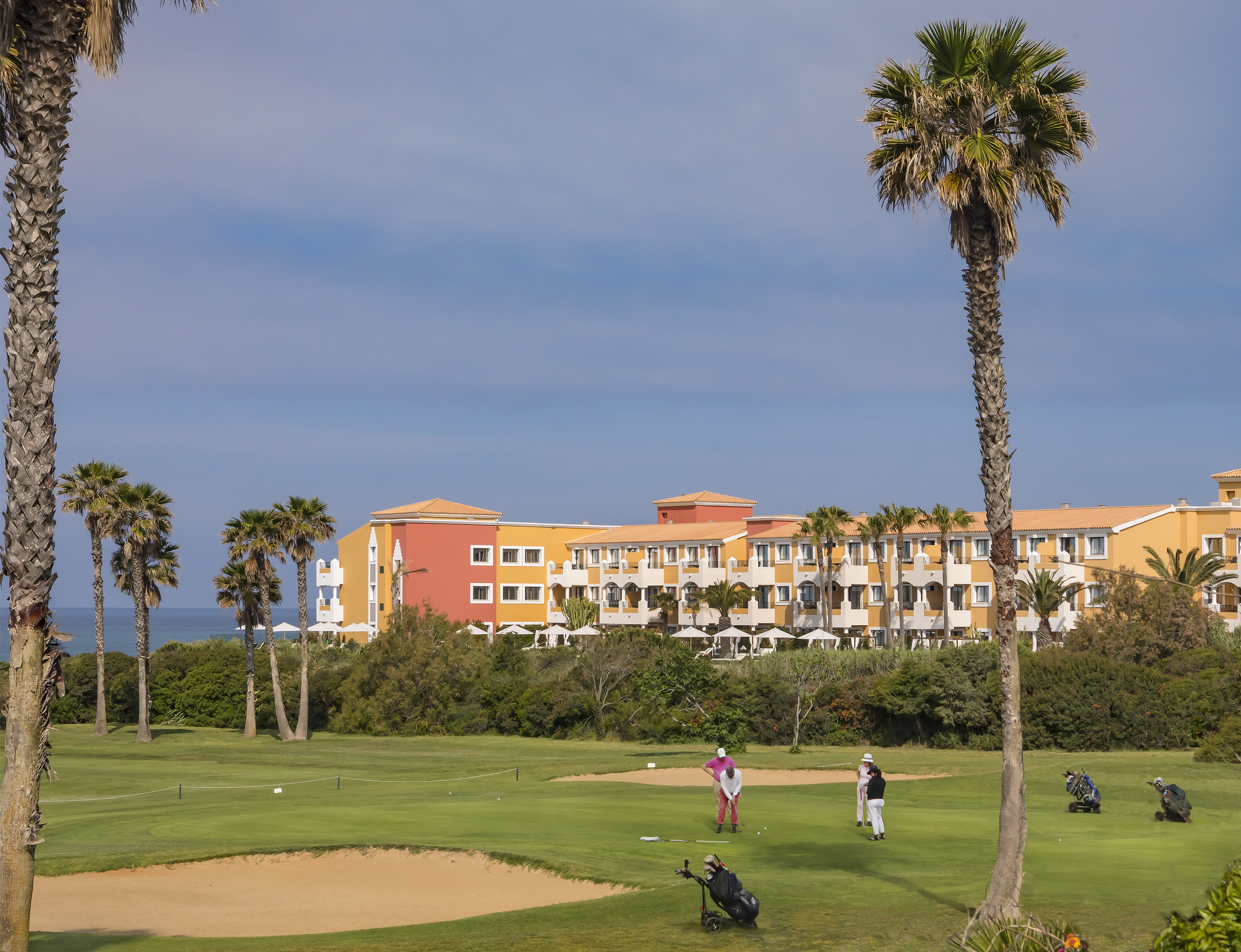 Golfers on tropical golf course with colorful resort hotel and palm trees.