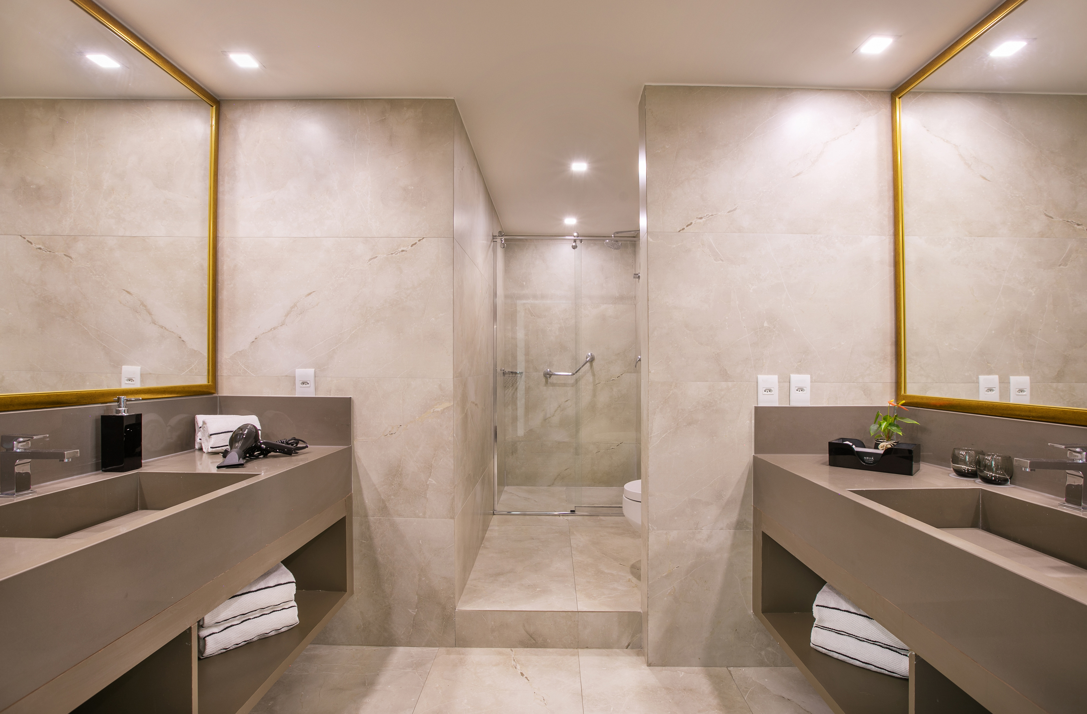 Modern bathroom with dual vanities, gold-framed mirrors, and a glass shower.