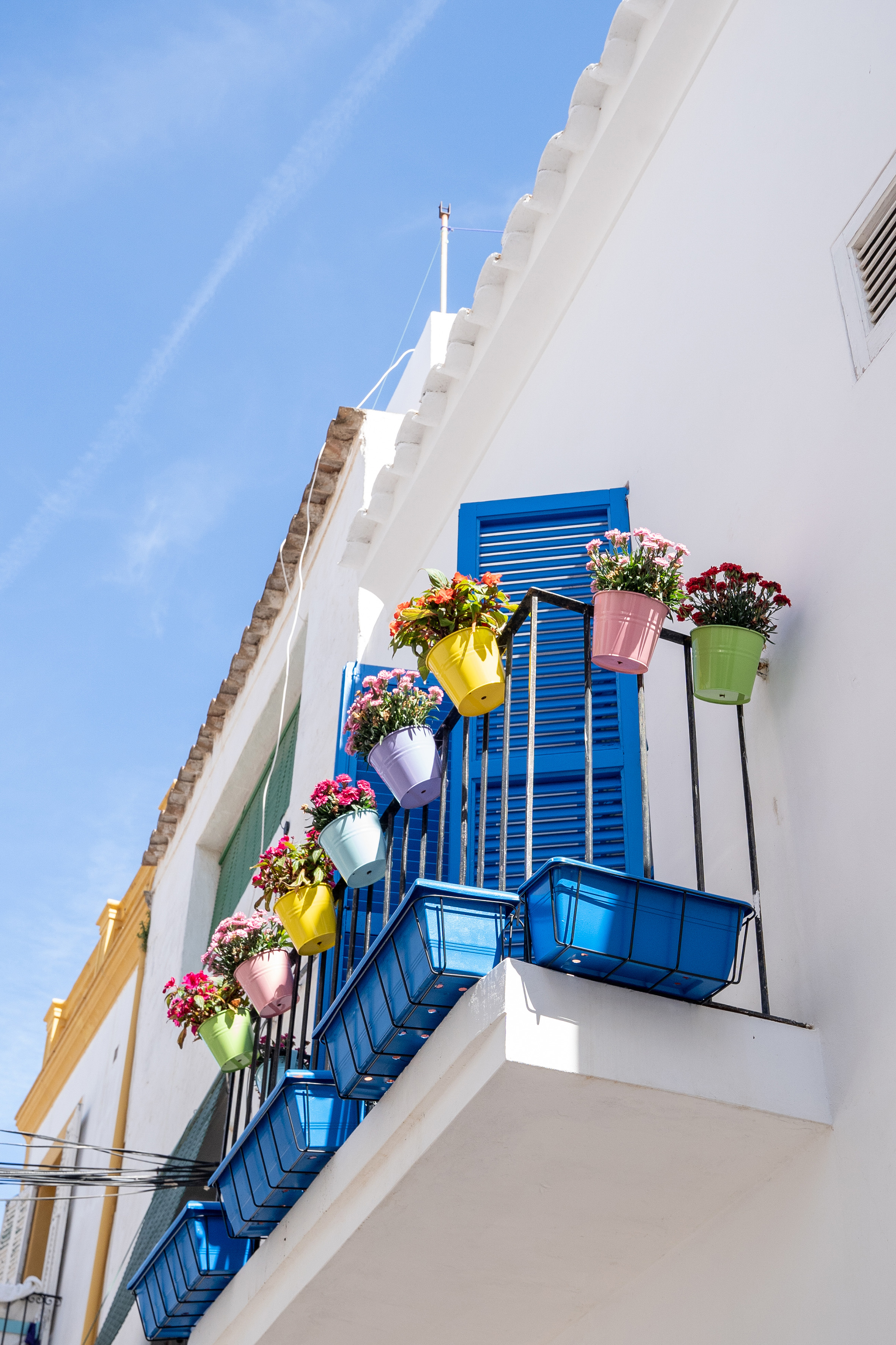 White Mediterranean balcony with blue shutters and vibrant flower pots.