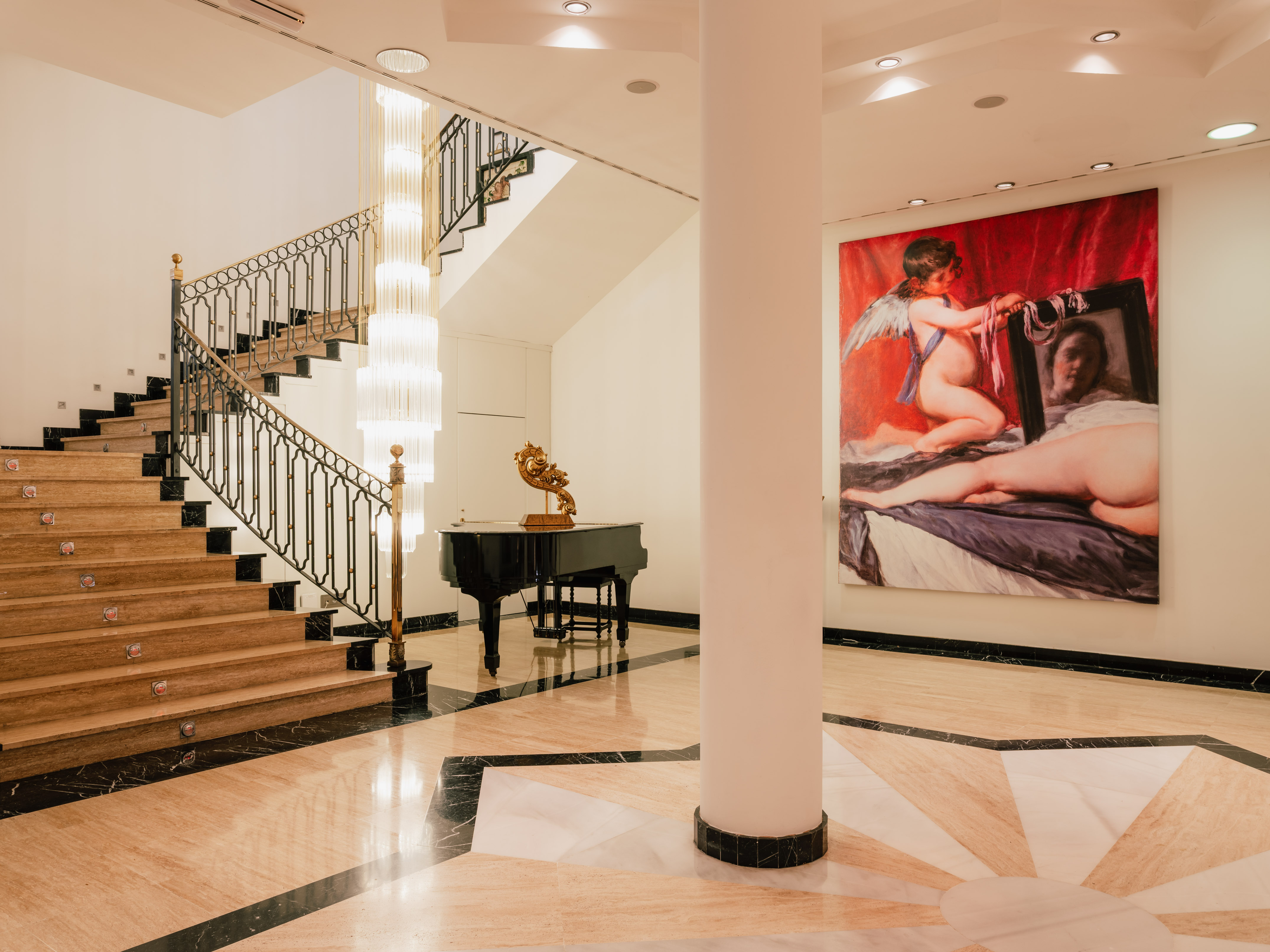 Grand foyer with marble staircase, chandelier, piano, and classical art.