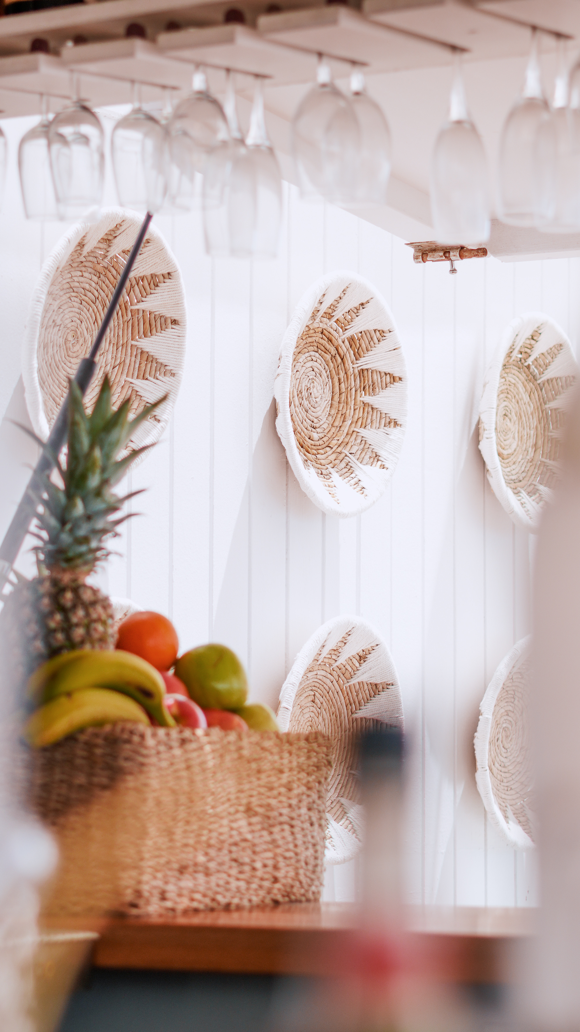 Decorative woven plates, fresh fruit basket, and hanging wine glasses.