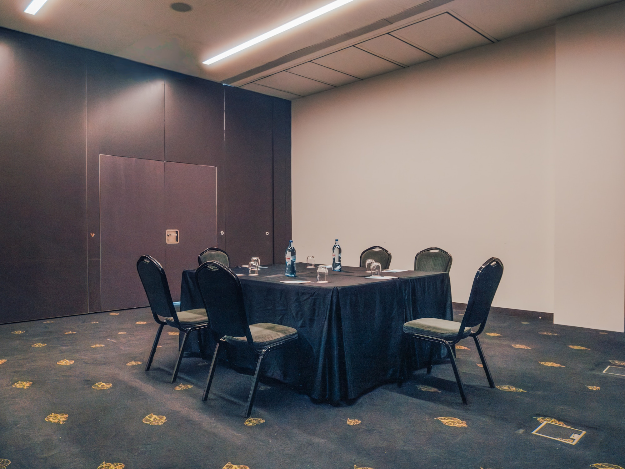 Empty conference room with black square table, chairs, and bottled water.