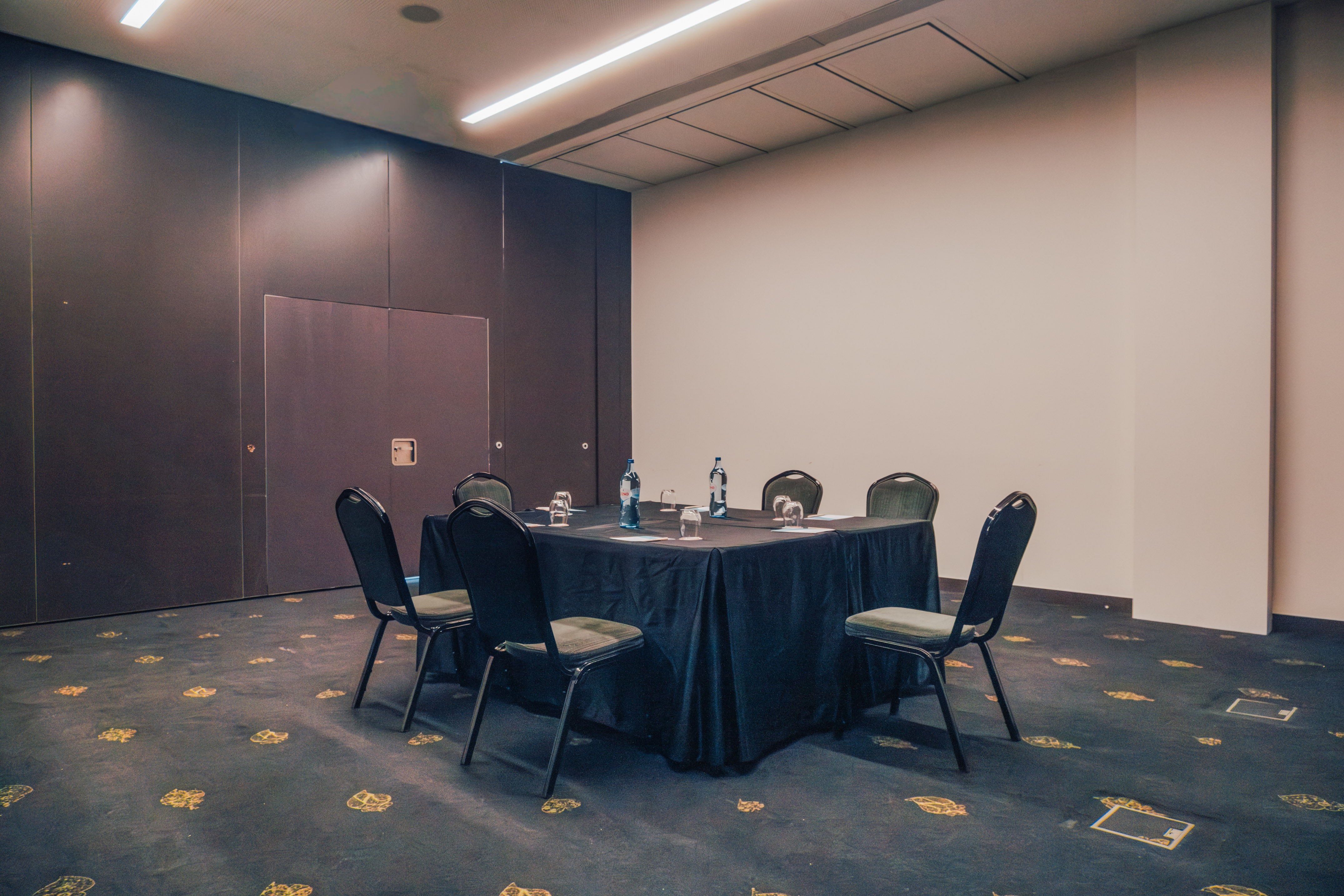 Empty conference room with black square table, chairs, and bottled water.