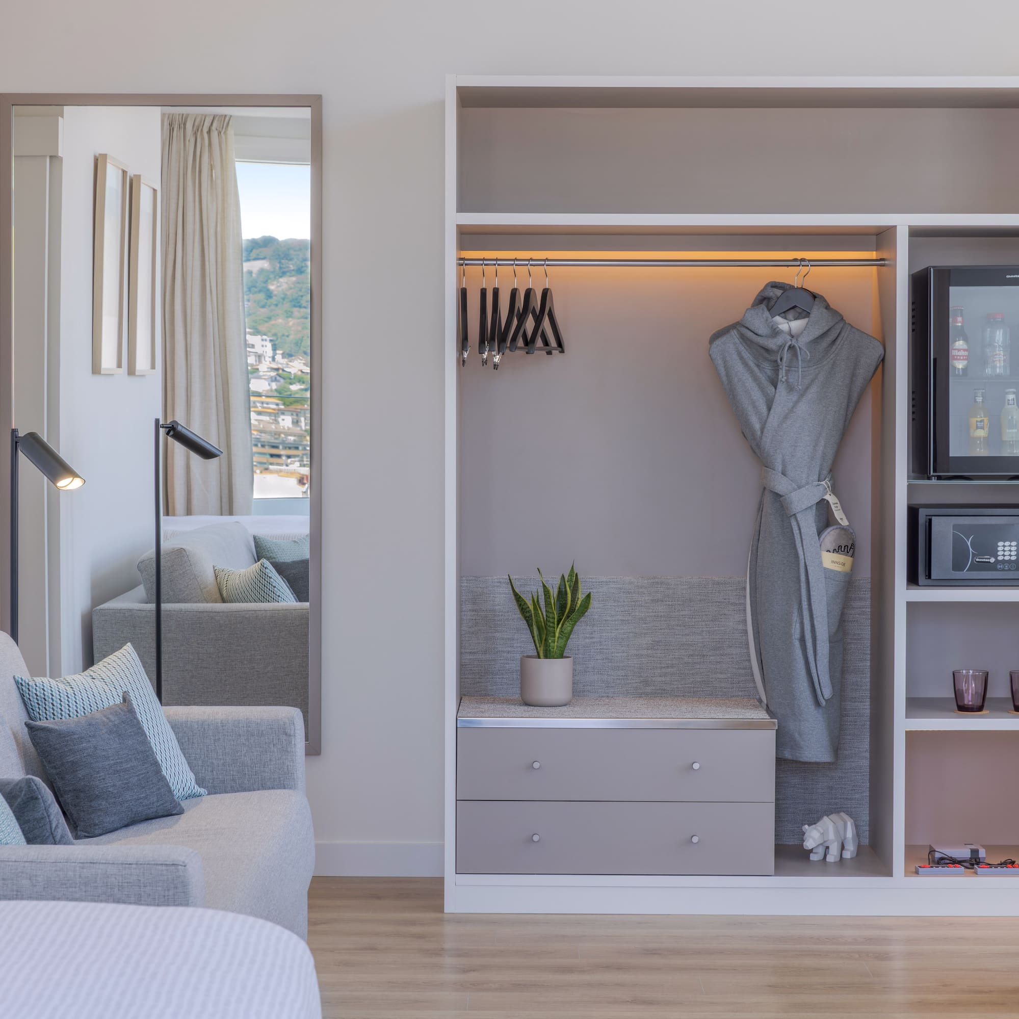 Interior de habitación de hotel moderna con sofá, armario, minibar y espejo.