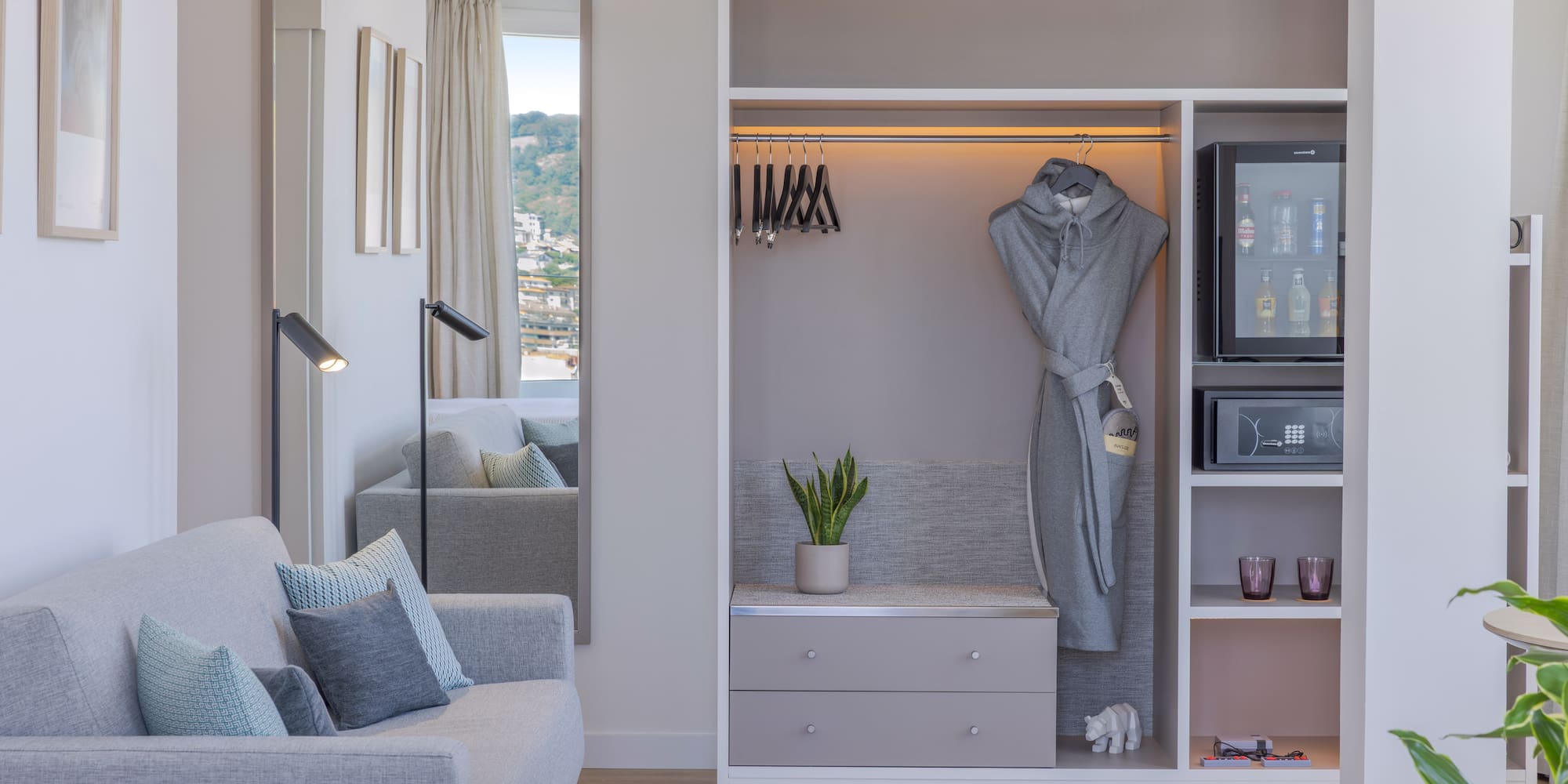 Interior de habitación de hotel moderna con sofá, armario, minibar y espejo.