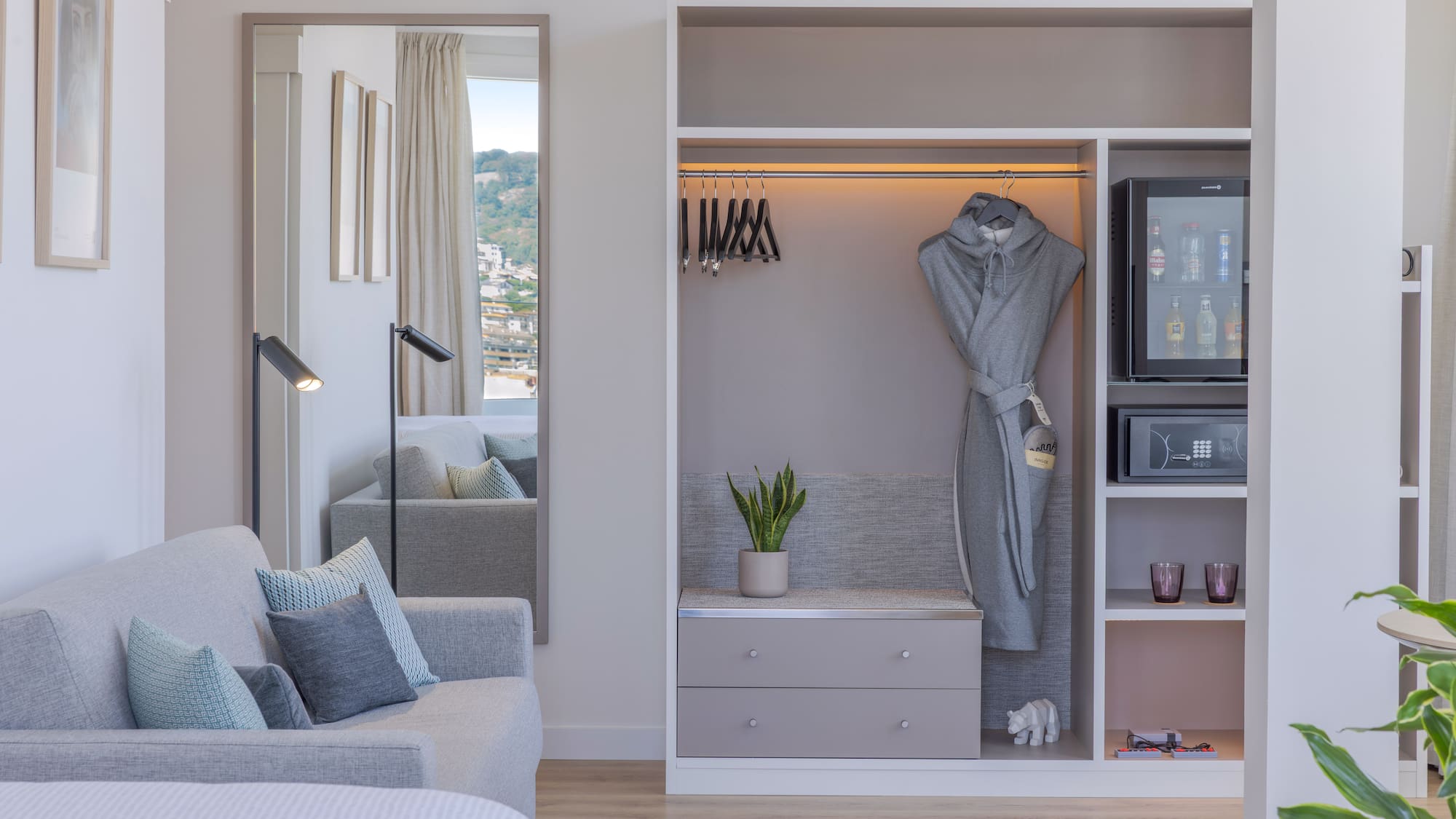 Interior de habitación de hotel moderna con sofá, armario, minibar y espejo.