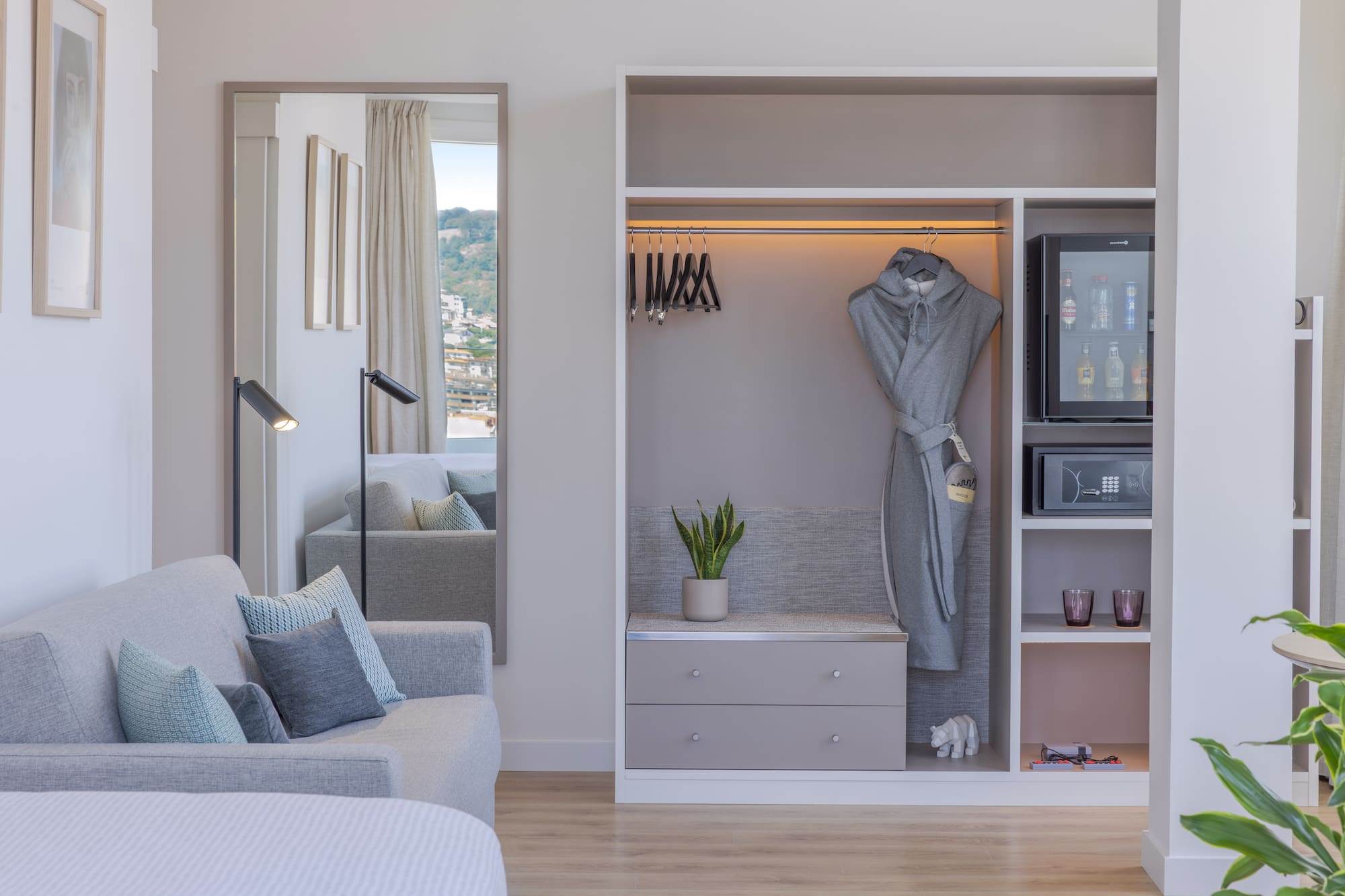 Interior de habitación de hotel moderna con sofá, armario, minibar y espejo.