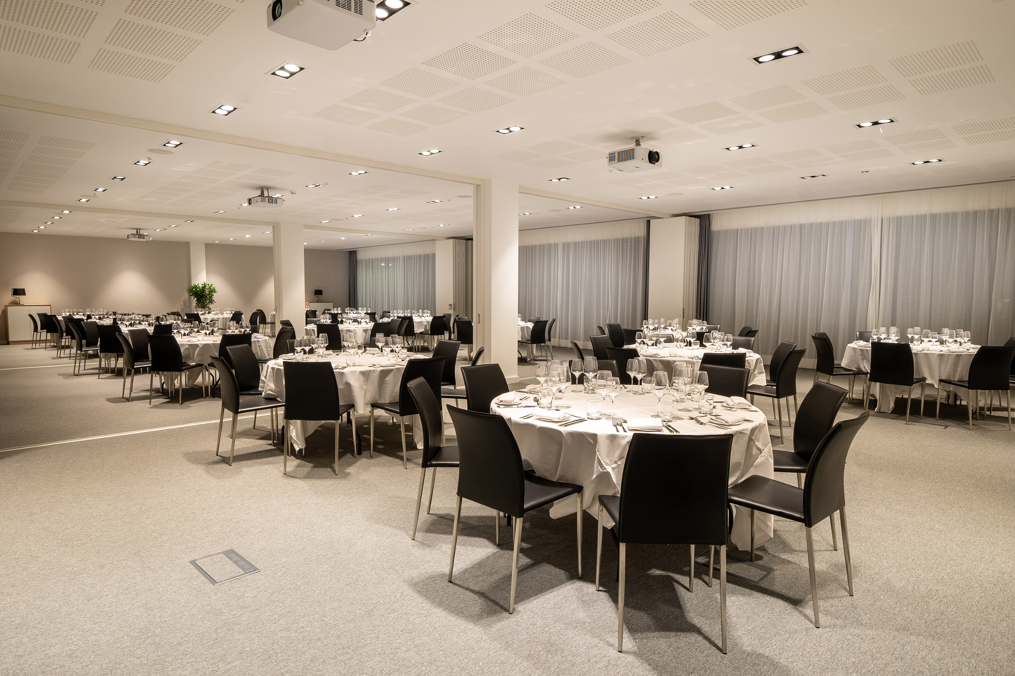 Spacious banquet hall with round tables, black chairs, and white tablecloths.