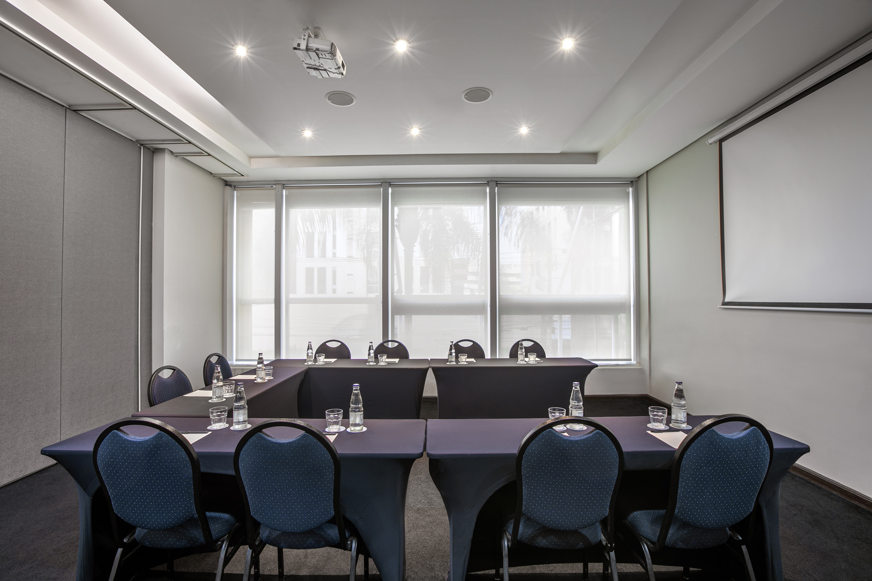 Professional conference room with U-shaped table, projector, and screen.