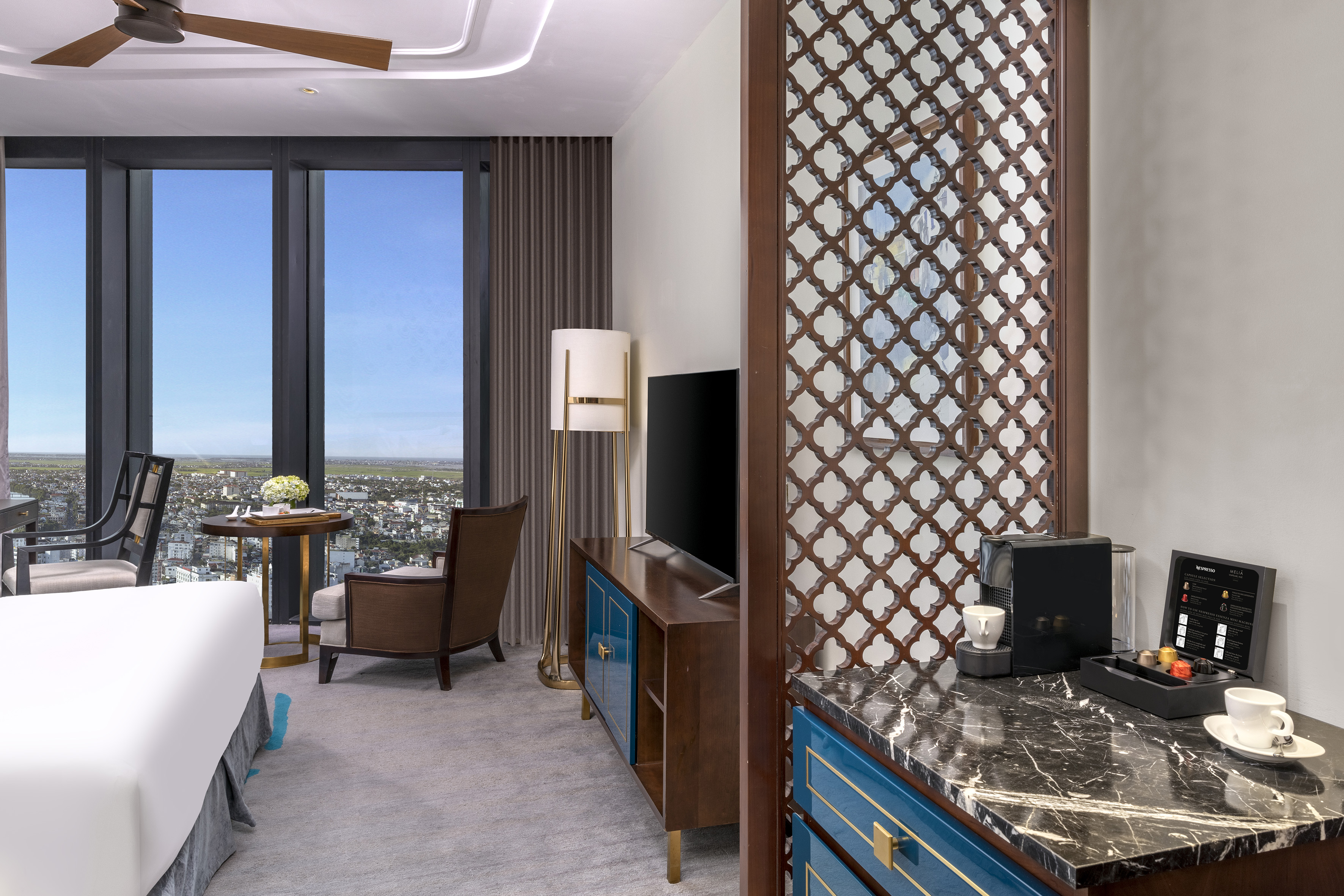 Luxury hotel room with city view, modern decor, Nespresso machine, wooden screen.