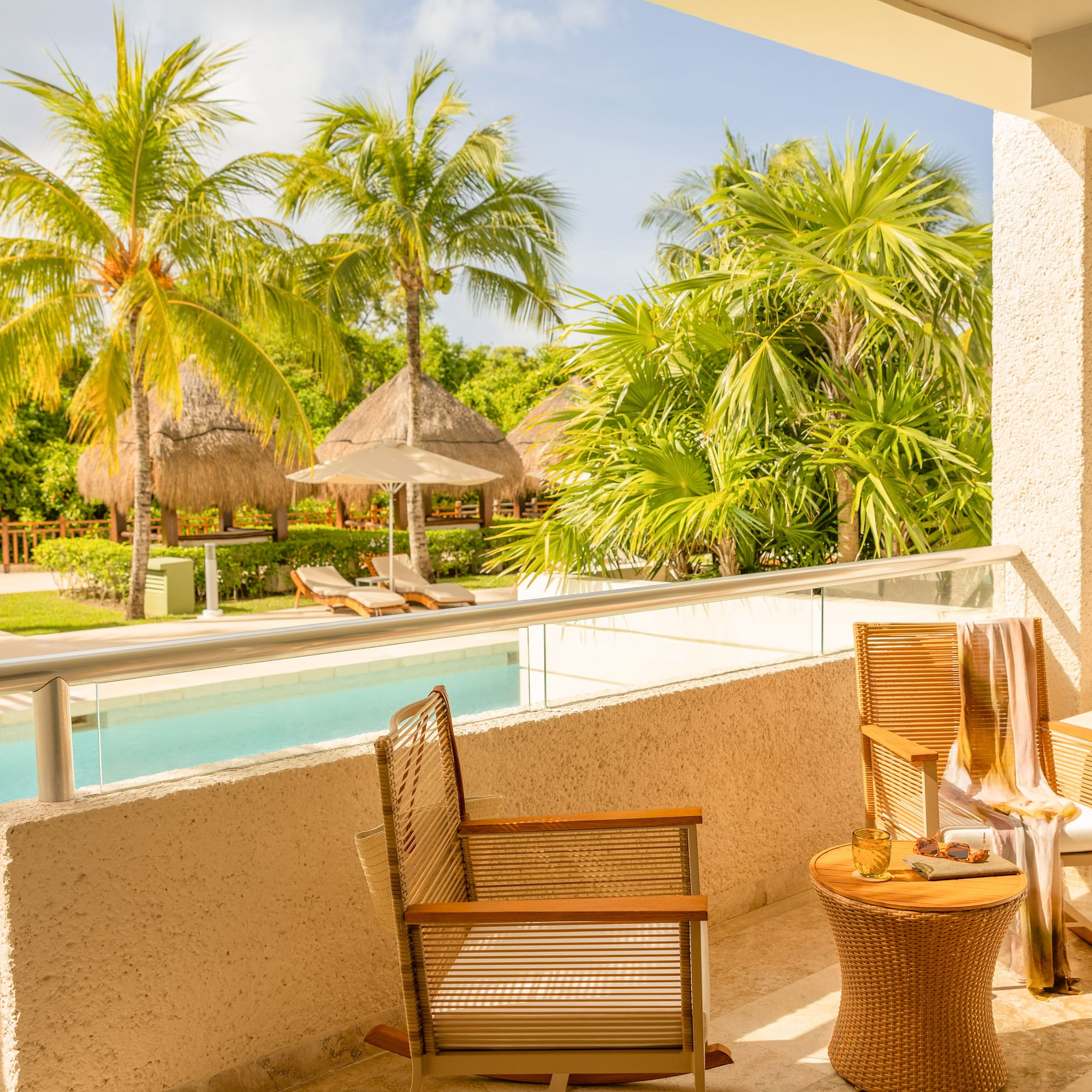Tropical resort balcony with private jacuzzi, pool view, and palm trees.