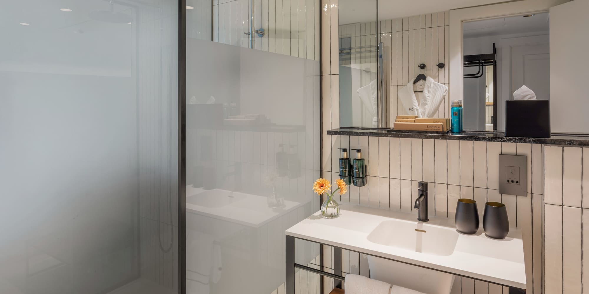 Modern hotel bathroom with walk-in rain shower, white vanity, and black accents.