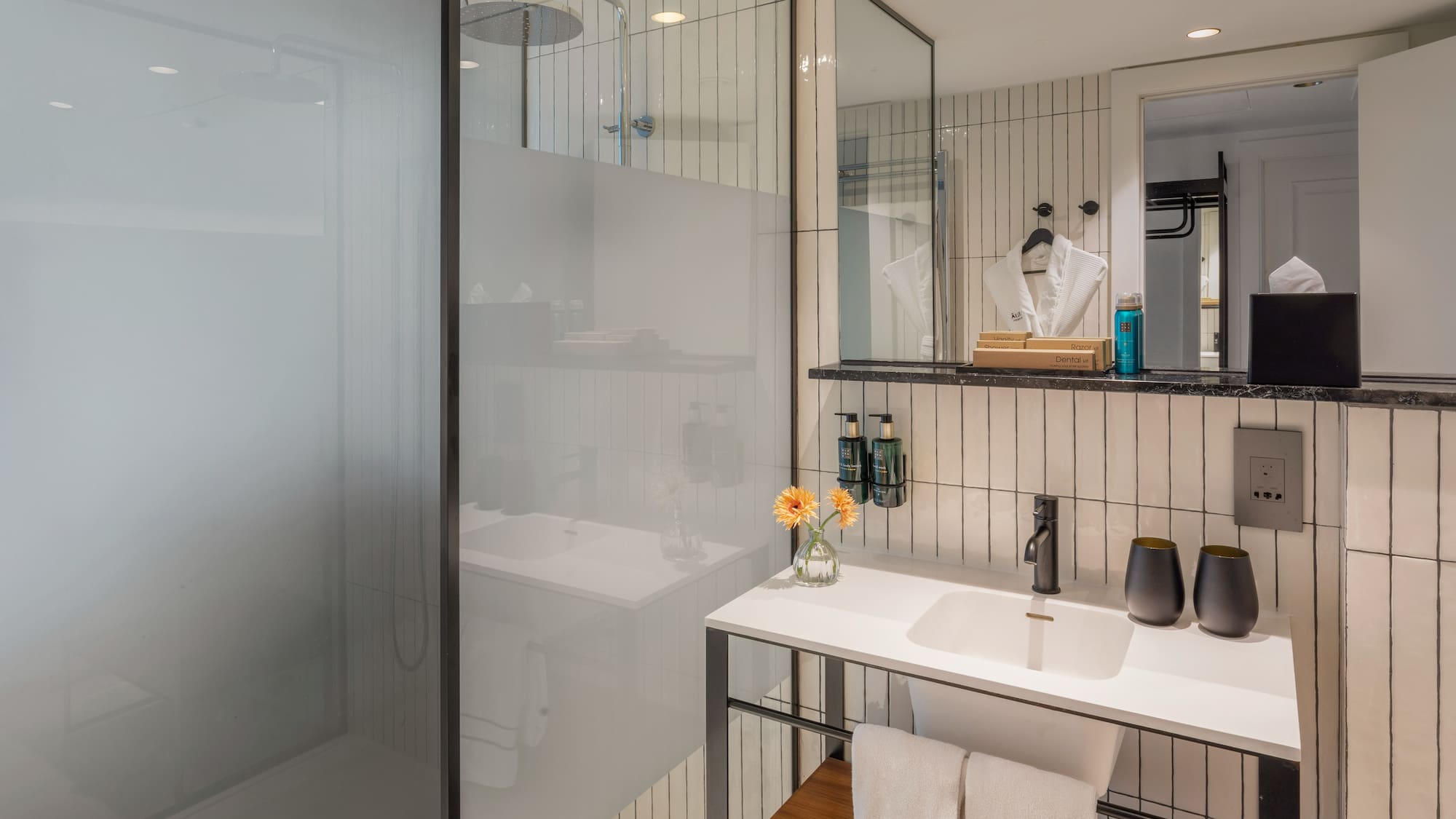 Modern hotel bathroom with walk-in rain shower, white vanity, and black accents.