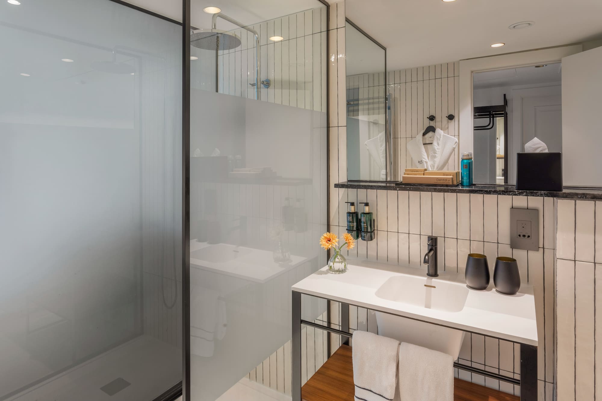 Modern hotel bathroom with walk-in rain shower, white vanity, and black accents.