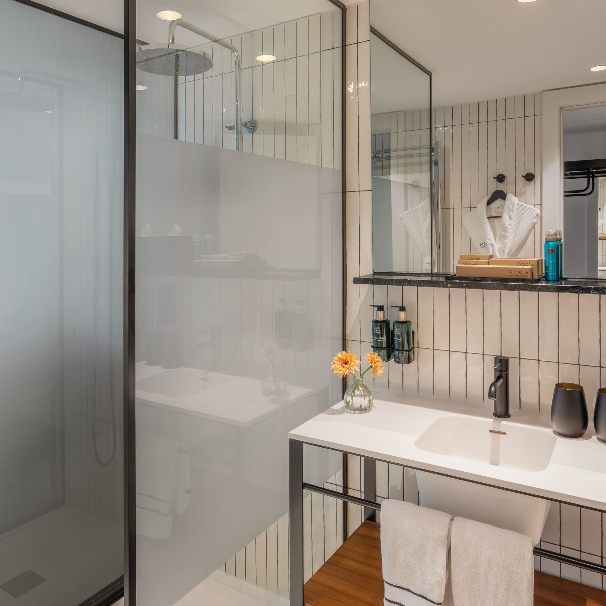 Modern hotel bathroom with walk-in rain shower, white vanity, and black accents.
